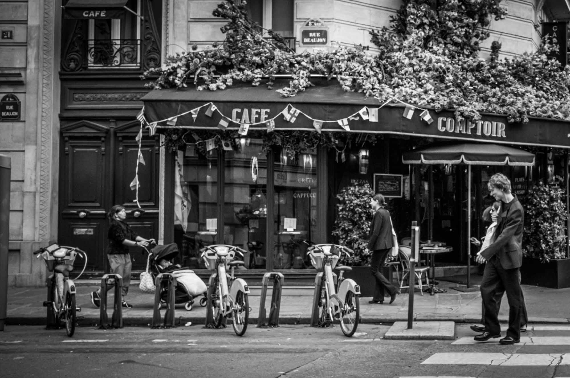 Black and white photo of a Parisian café with bicycles and pedestrians on Rue Beaujolais.