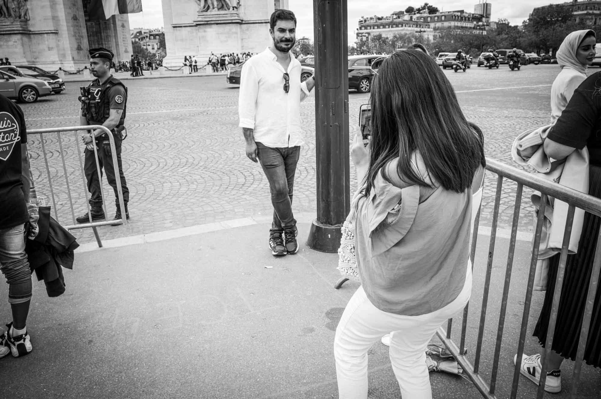 Tourists take photos near the Arc de Triomphe in black and white street scene.