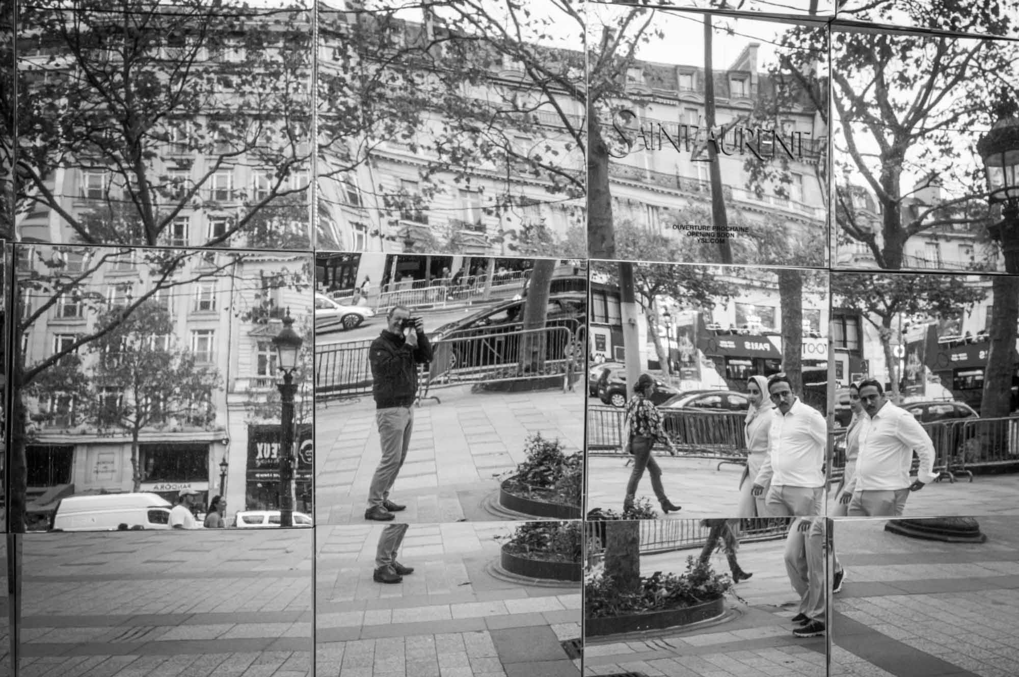 Mirrored street reflections with people walking in a bustling city scene, capturing urban life in black and white.