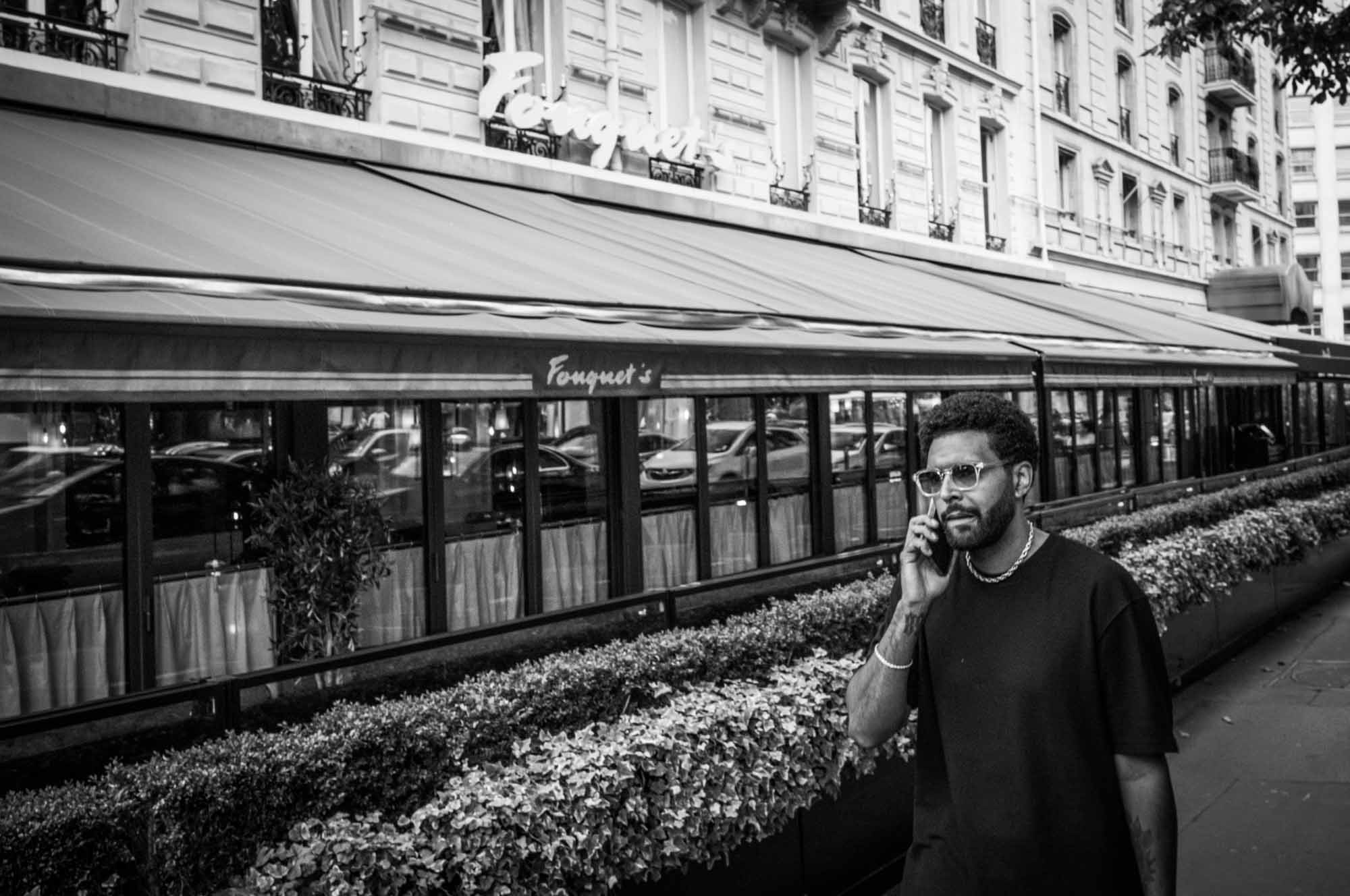 Man on phone walks past historic Fouquet's restaurant in urban setting.