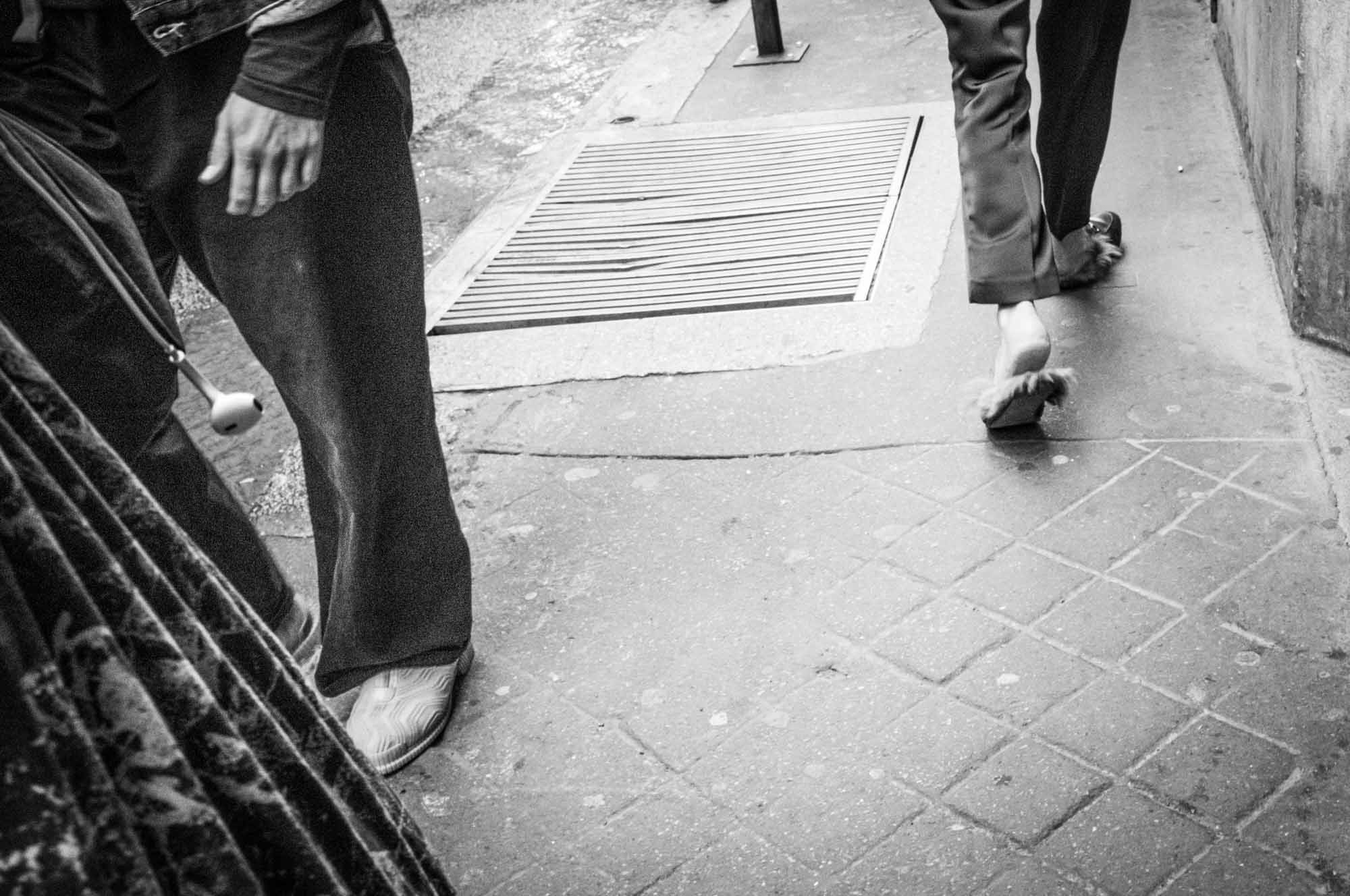 Street style footwear: person walking with unique fur sandals on a city sidewalk, monochrome photography.
