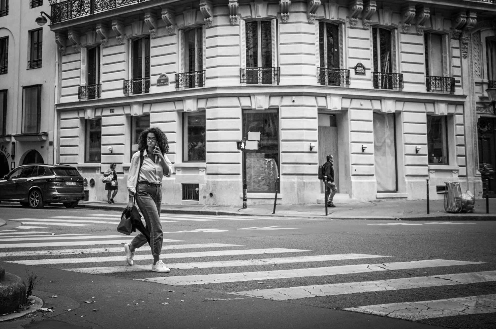 Urban crosswalk with people walking by classic architecture building in black and white.