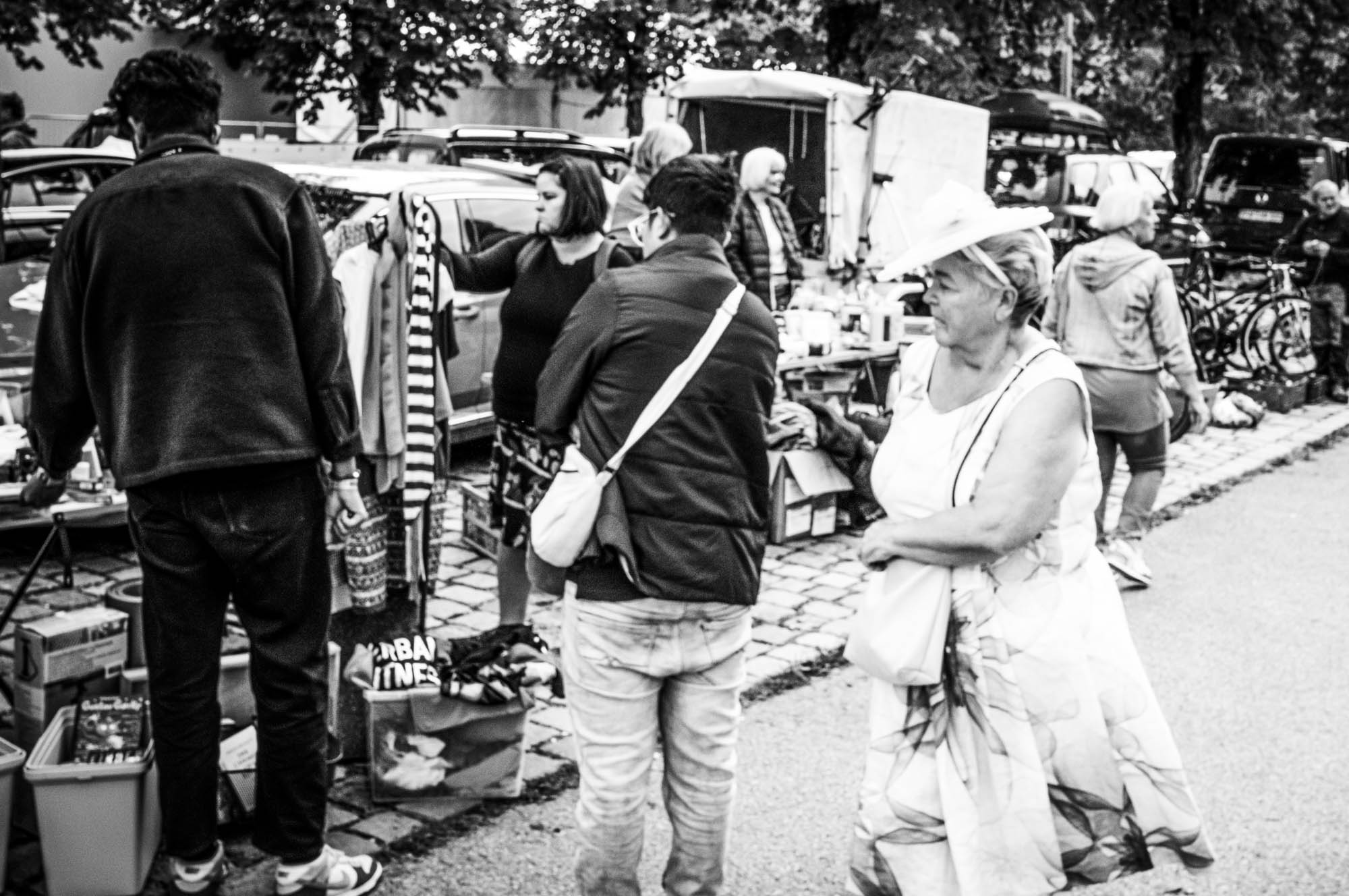 Black and white photo of people shopping at an outdoor market with various stalls and items.