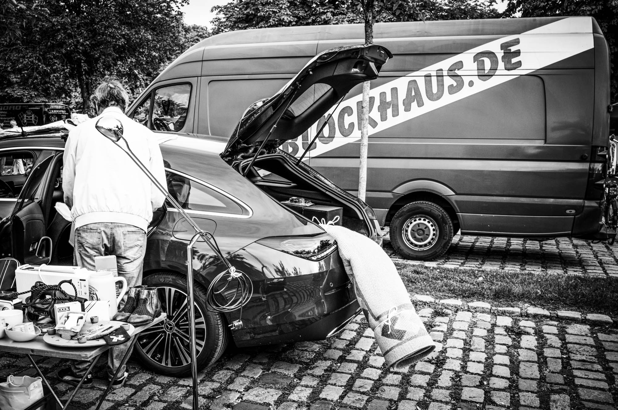 Man arranging items in car boot at outdoor market, with van in background.