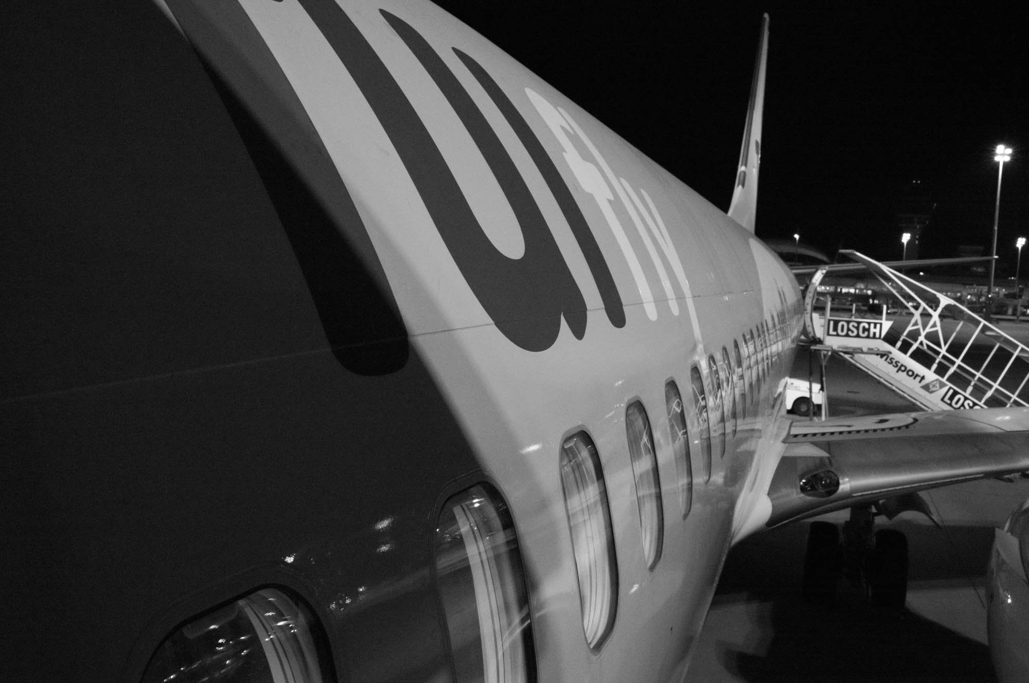 Black and white photo of an airplane parked at night with stairway access on the tarmac.