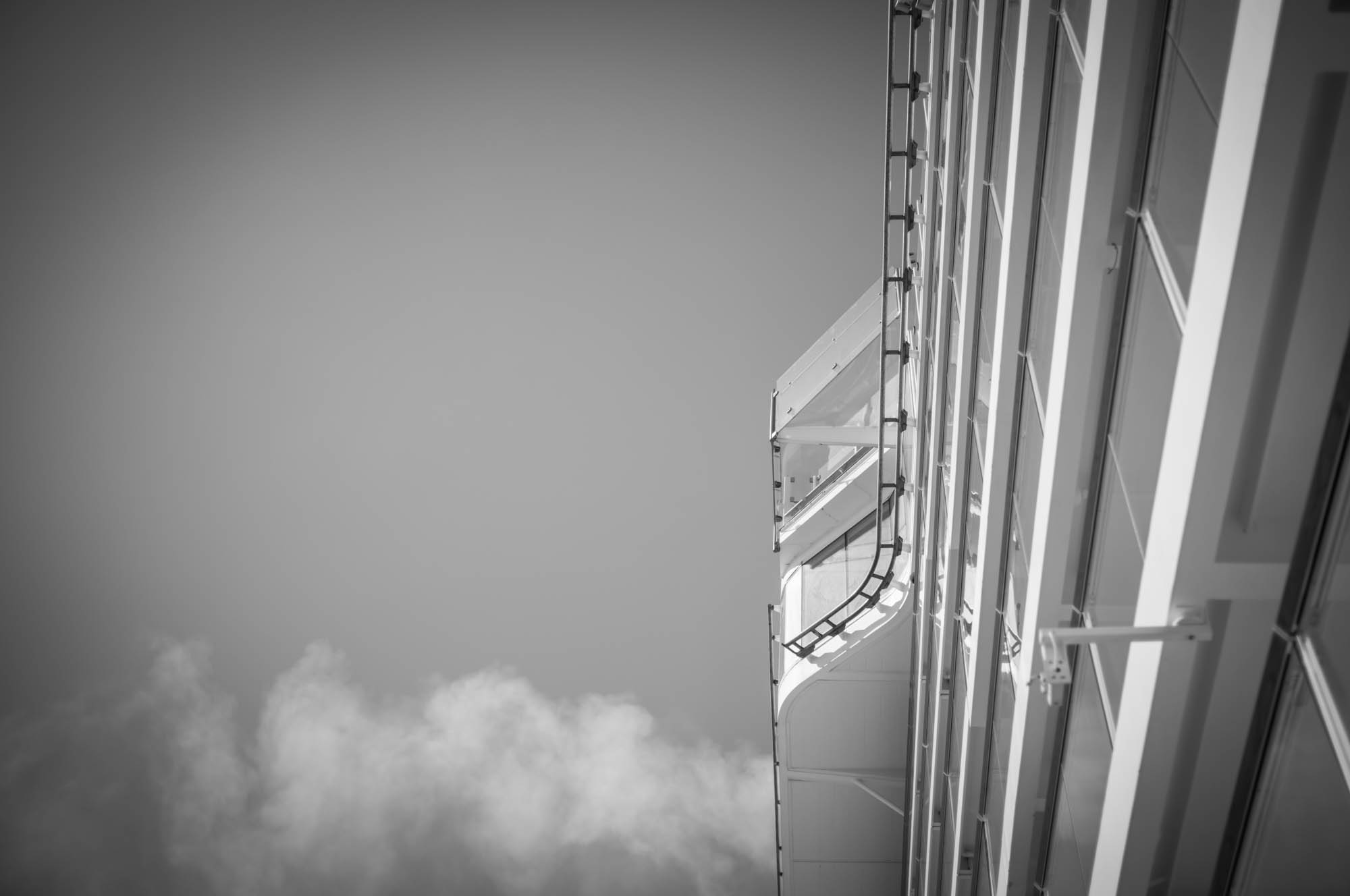 Black and white image of a ship's deck with clear sky and a hint of clouds, highlighting modern architectural details.