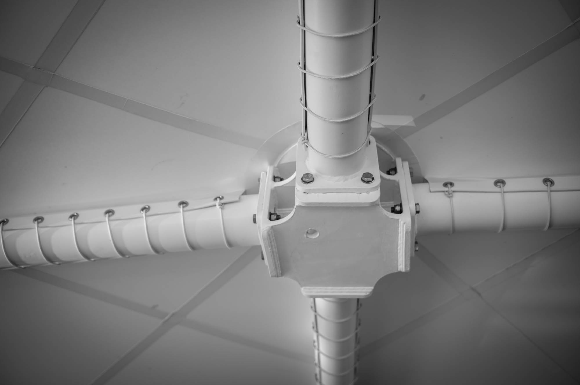 Close-up of industrial metal pipe connection on ceiling, showing bolts and structural details, in black and white.