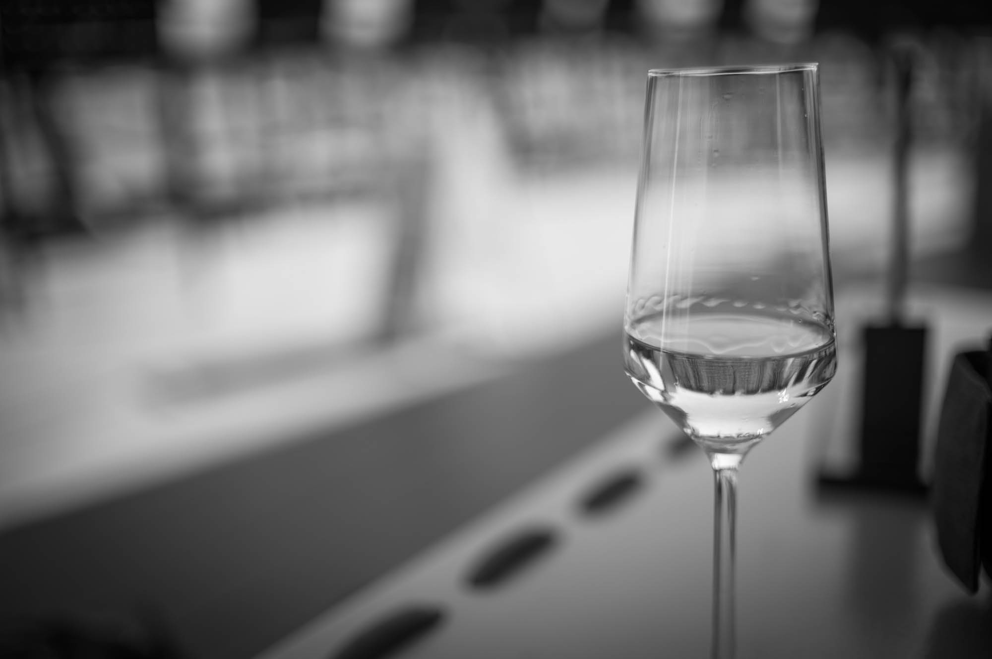 Black and white photo of a half-full wine glass on a blurred outdoor table setting.