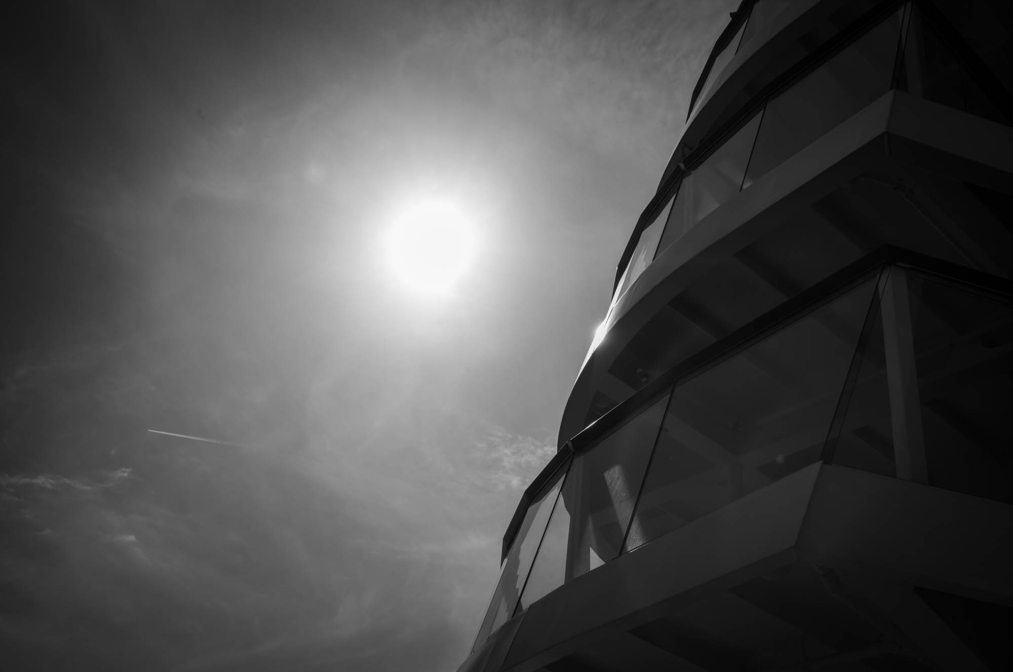 Black and white view of modern building against bright sun in overcast sky.