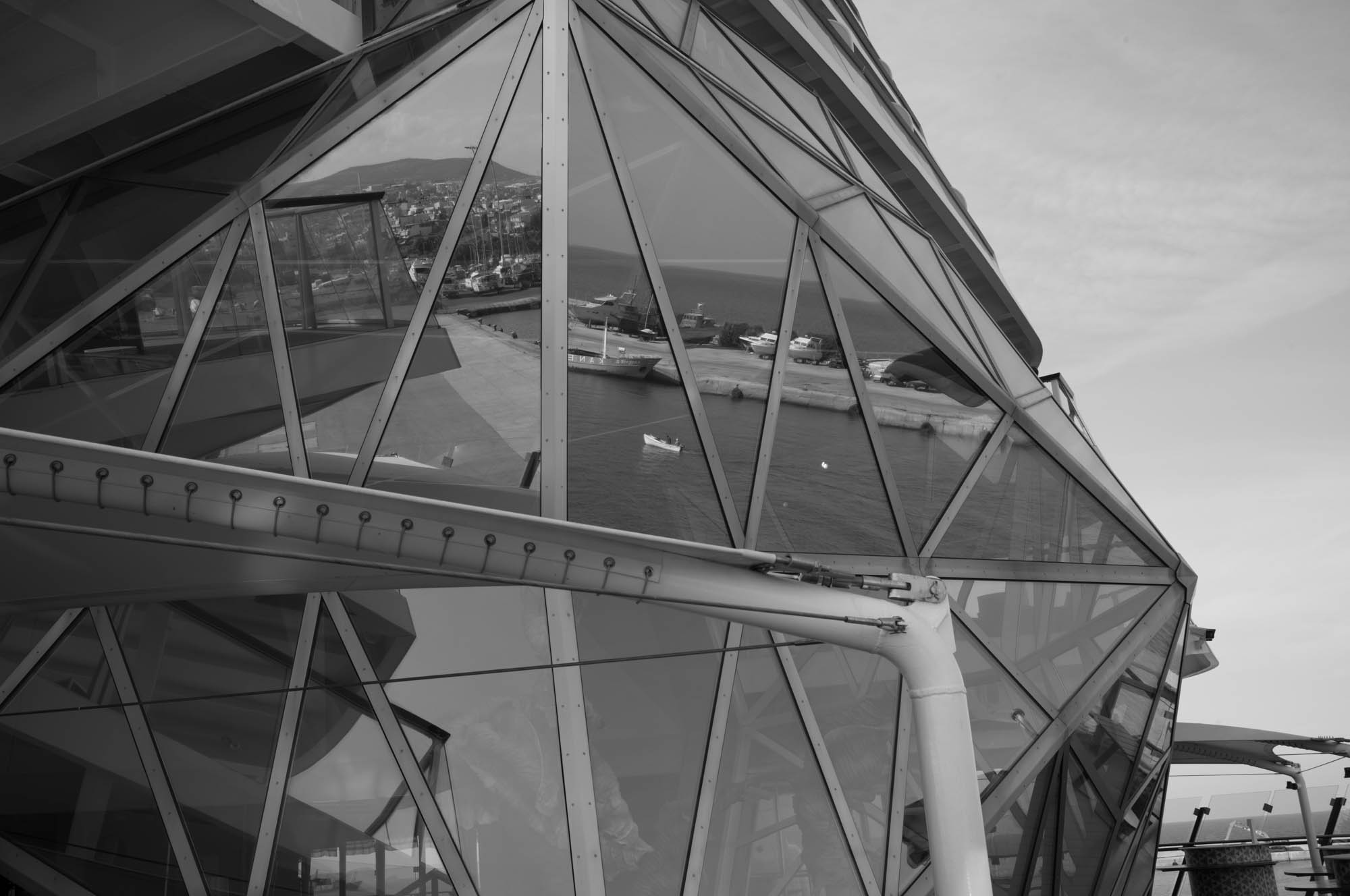 Modern geometric glass architecture reflecting a coastal harbor scene in black and white.