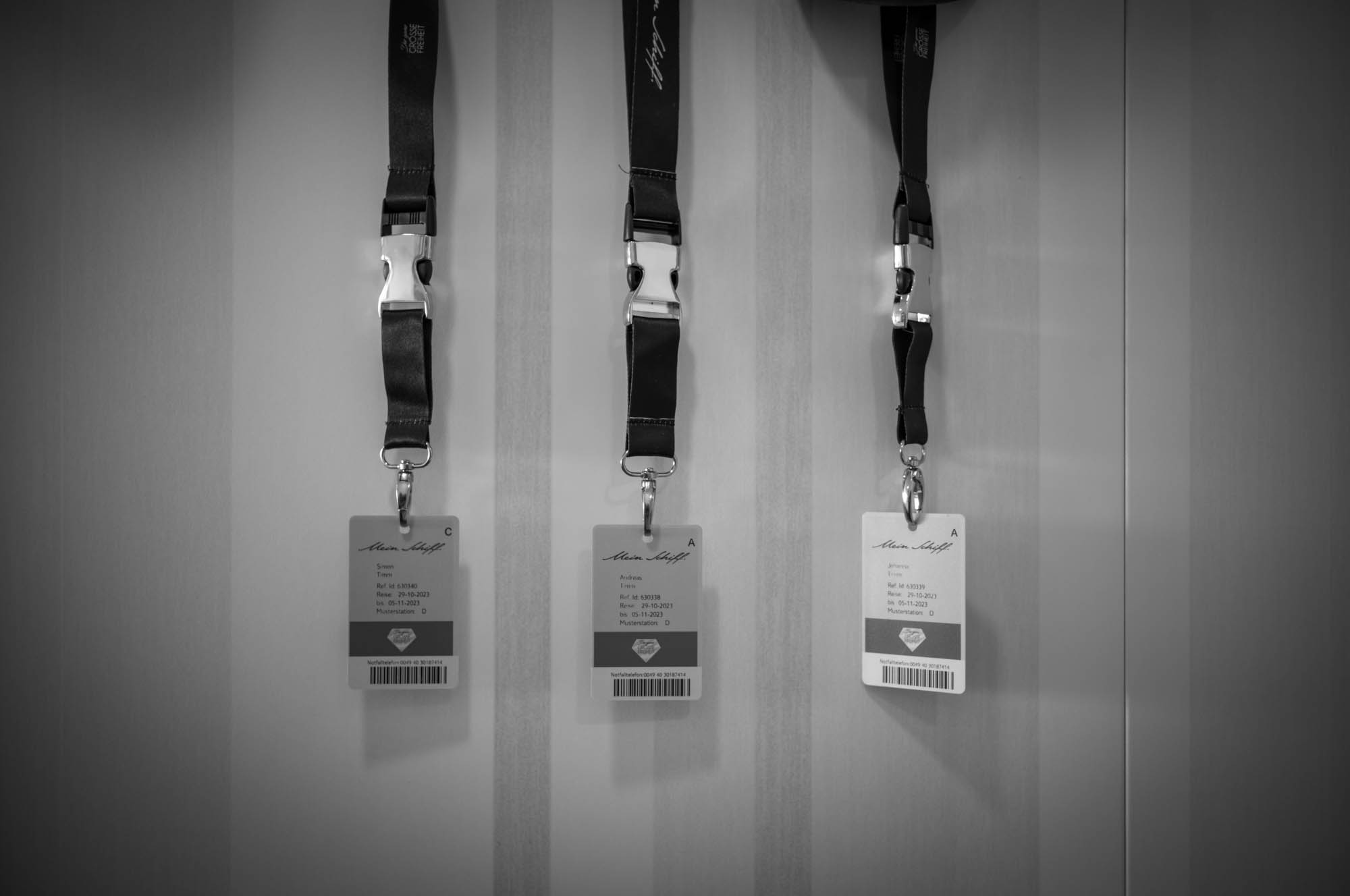 Black and white image of three hanging lanyards with ID cards on a striped wall background.