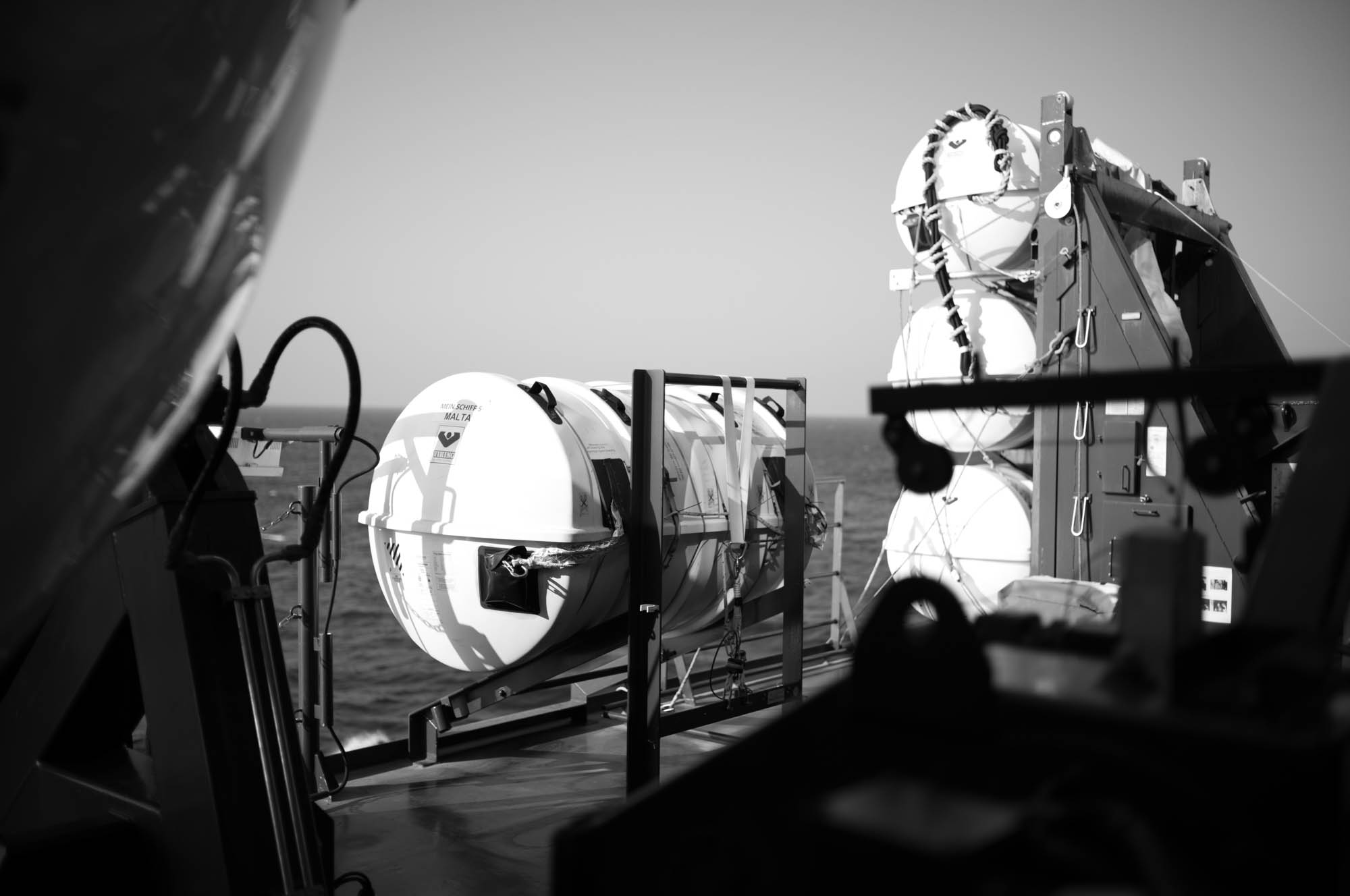 Black and white image of lifeboats on a ship deck, with ocean in the background.