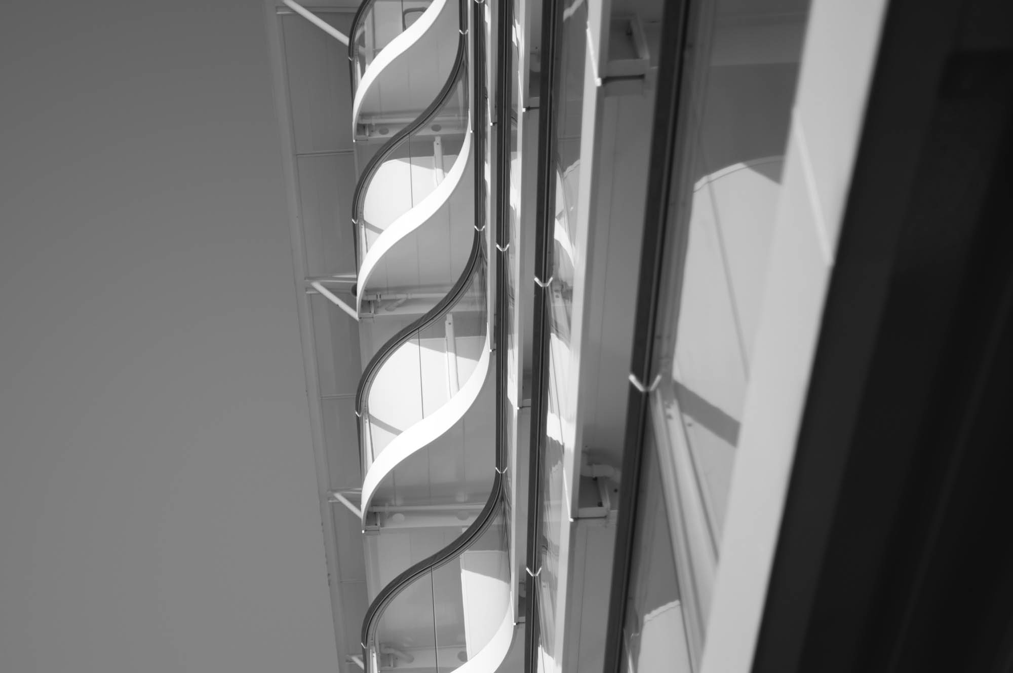 Close-up of modern architectural structure with curved metal and glass elements, in black and white.