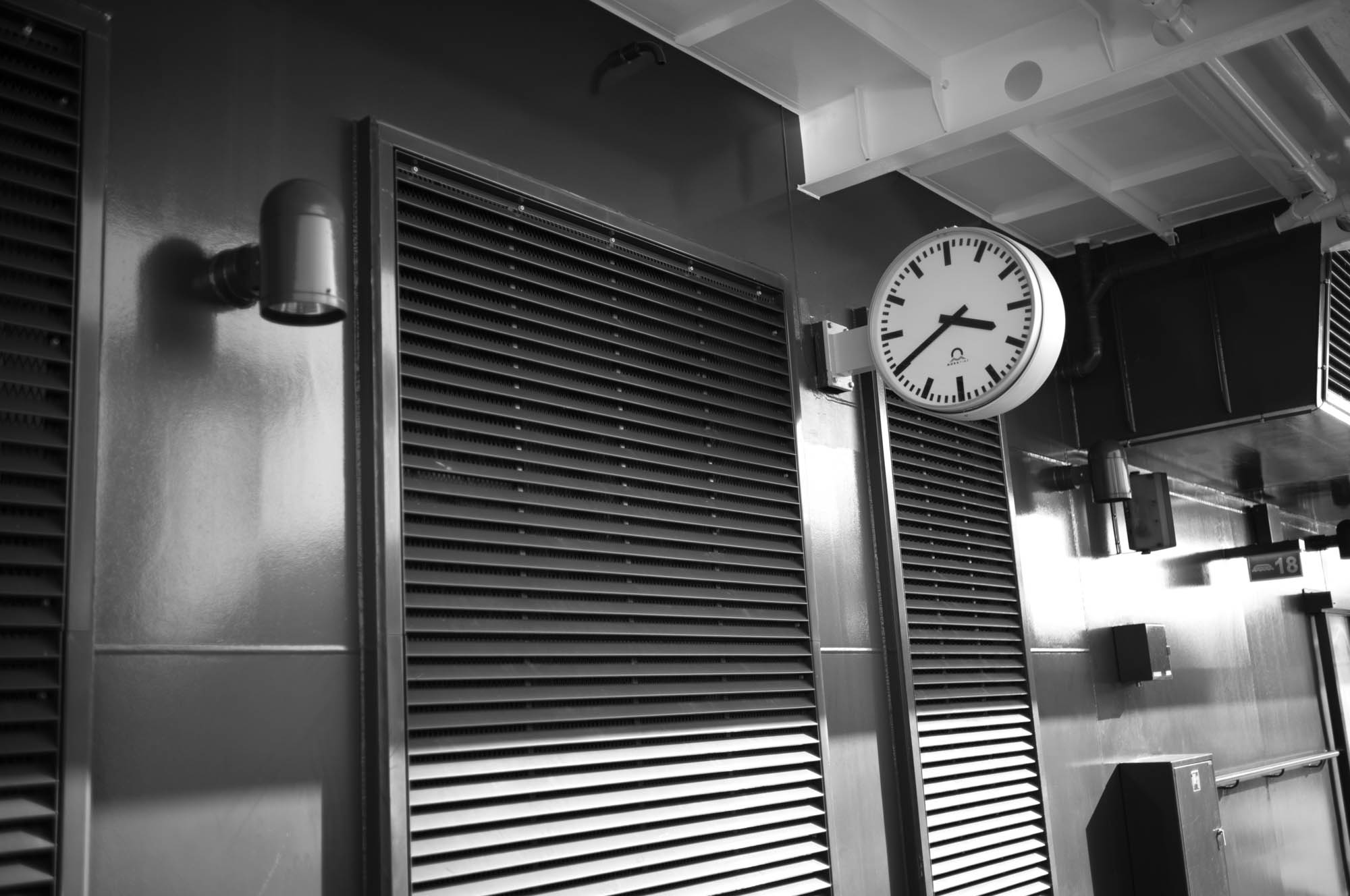 Black and white photo of a wall clock and industrial vents in a modern interior setting.