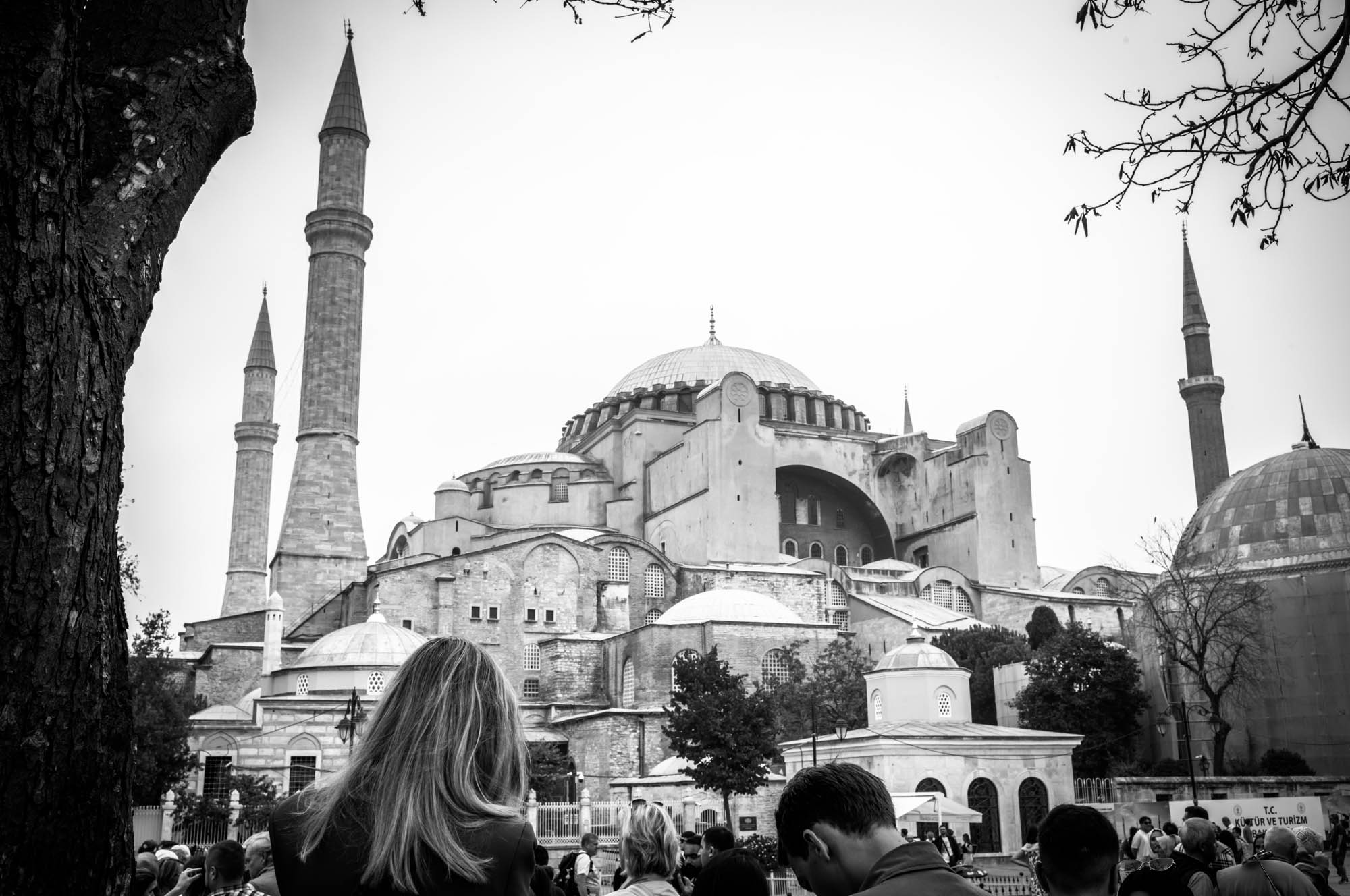 Black and white photo of Hagia Sophia in Istanbul with people in the foreground and tree branches framing the scene.