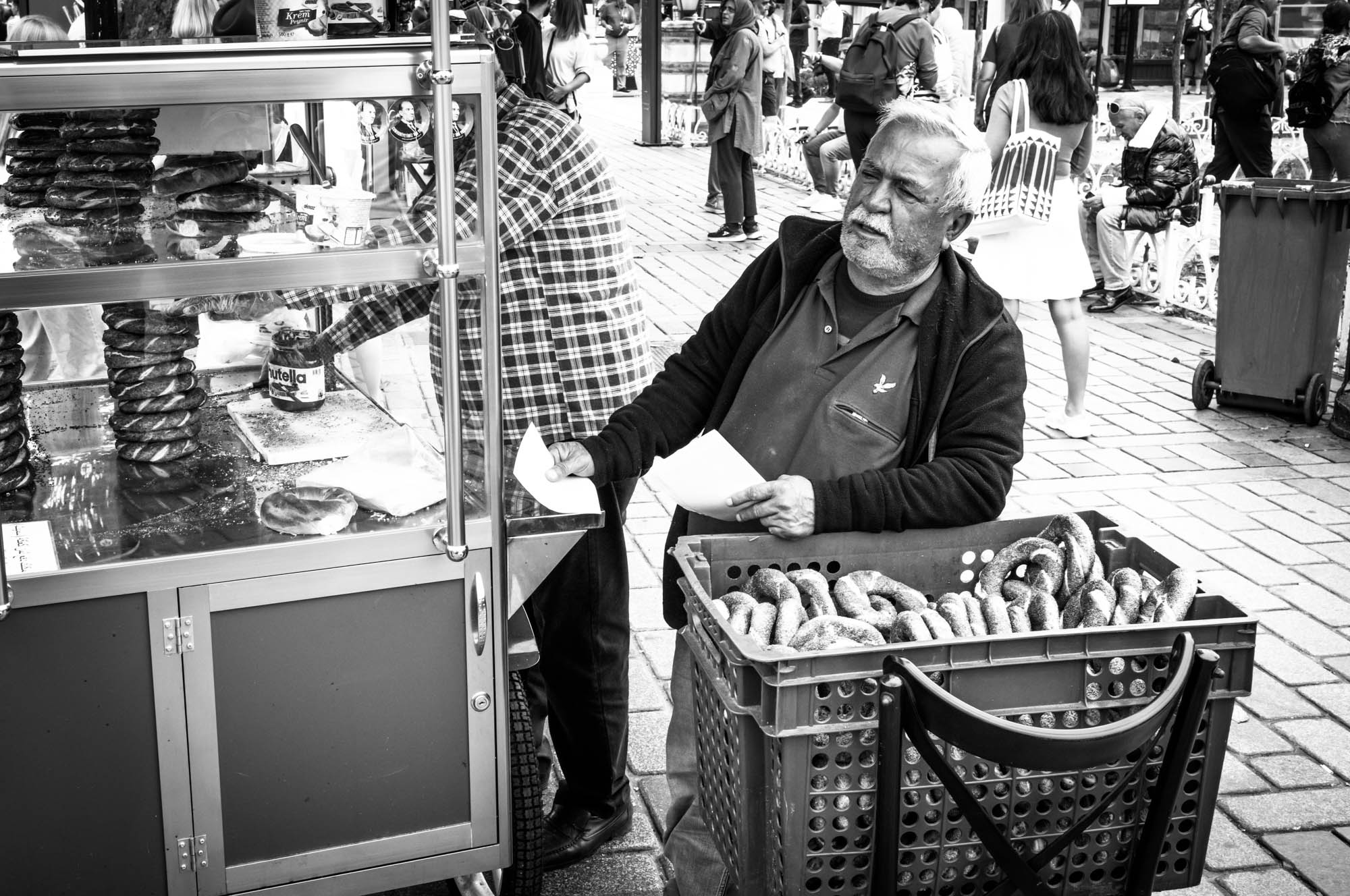 A street vendor selling fresh pretzels from a cart in a busy market area, surrounded by pedestrians.