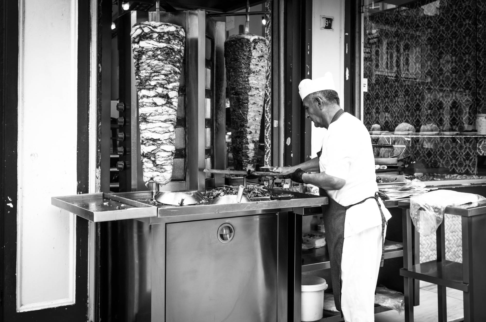 Chef preparing shawarma at an outdoor grill station in monochrome setting.