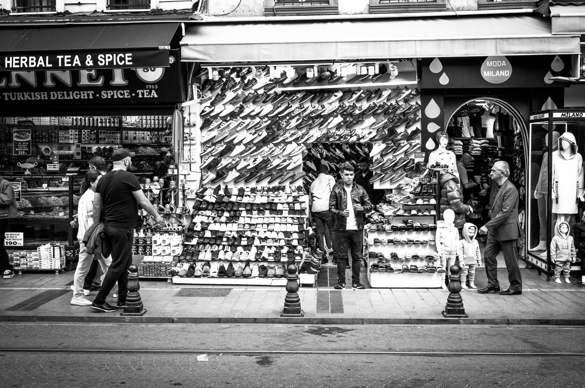 Black and white photo of bustling street market with shoe and clothing shops.