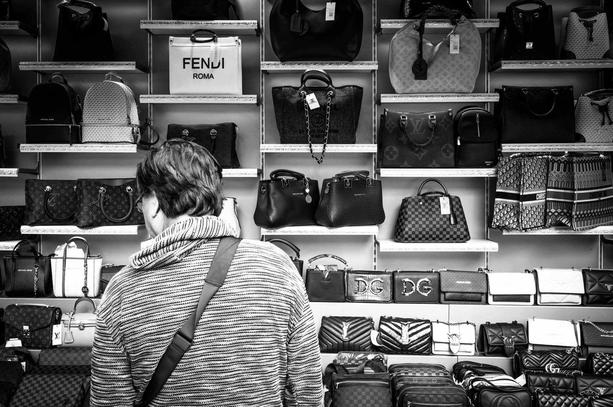 Person browsing shelves of designer handbags in a store.
