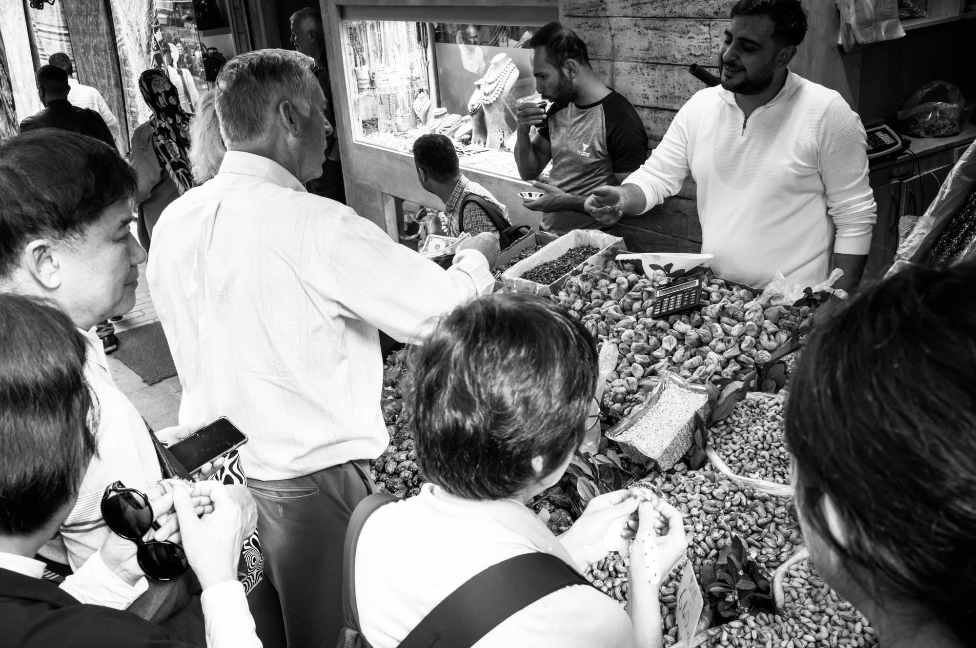 Shoppers at a vibrant street market buying dried fruits and nuts from a vendor.