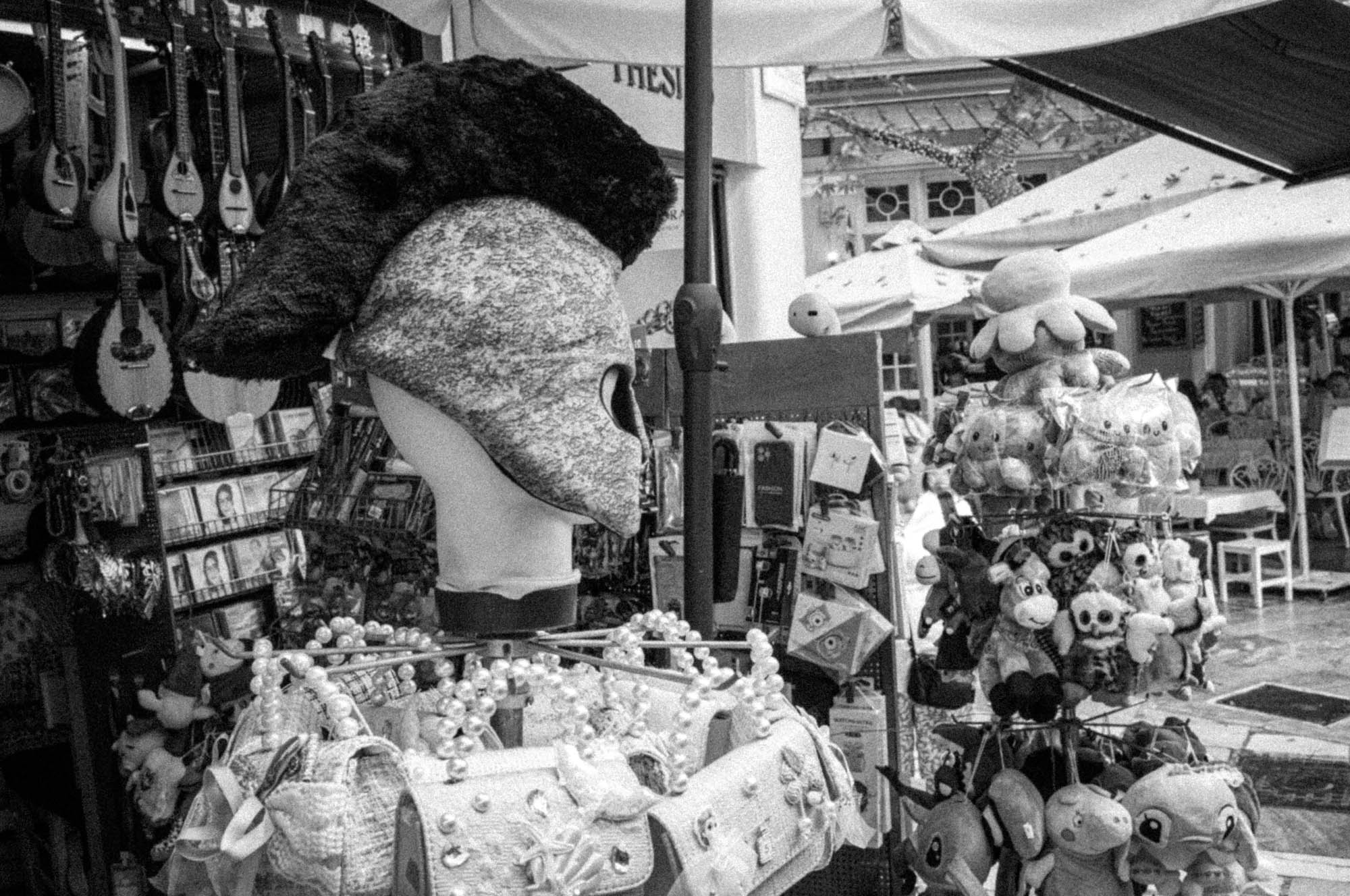 Street market stall selling plush toys, CDs, and decorative items under an umbrella in black and white.