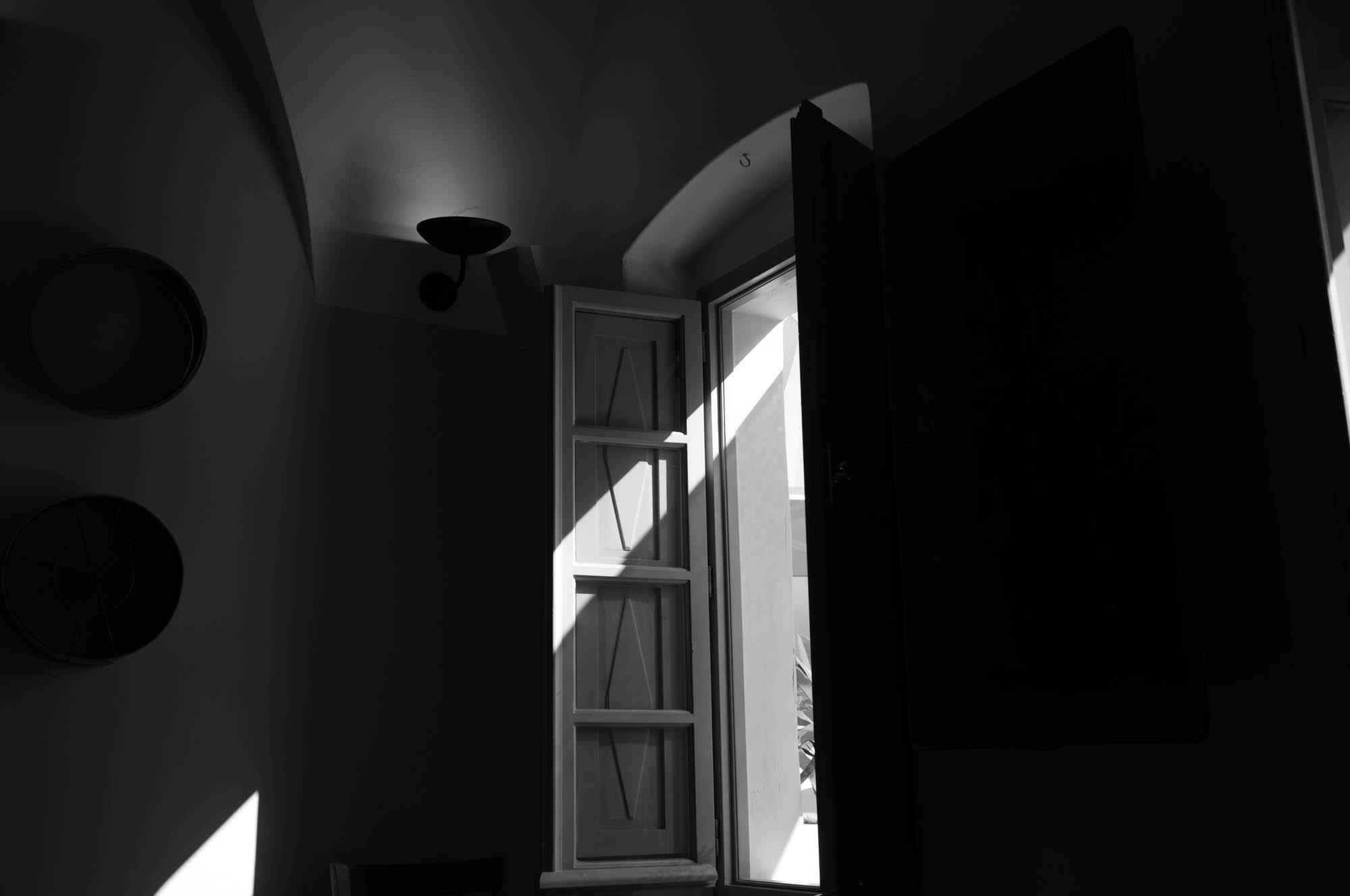Monochrome image of light streaming through an open window in a dark room, creating a dramatic shadow pattern.