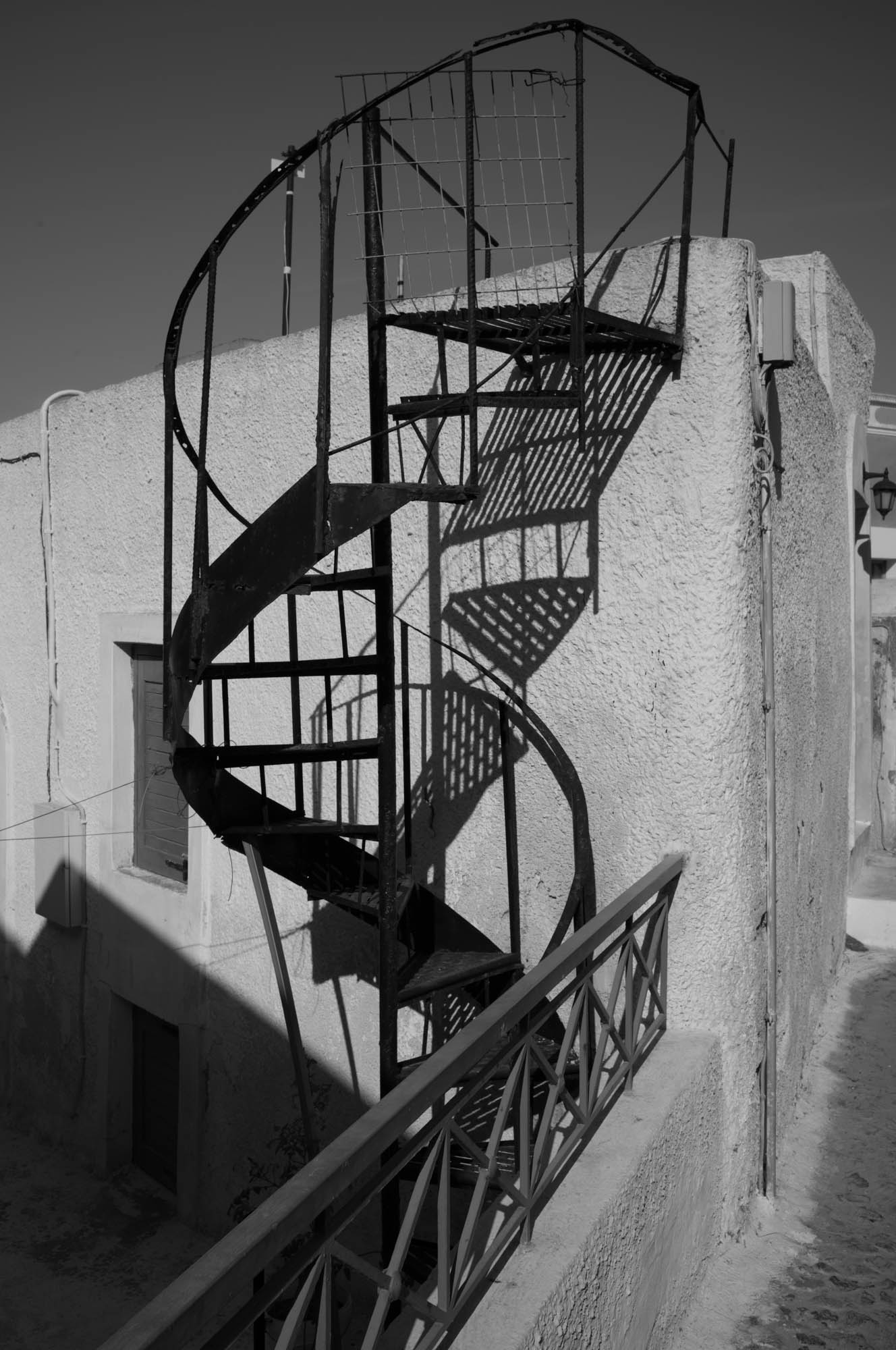 Black spiral staircase casting shadows on a textured wall in a monochrome setting.