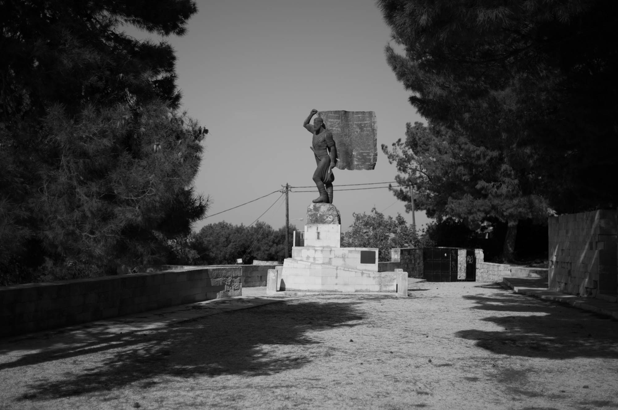 Monumental statue in a park setting, surrounded by trees, under a clear sky, evoking a sense of history and serenity.