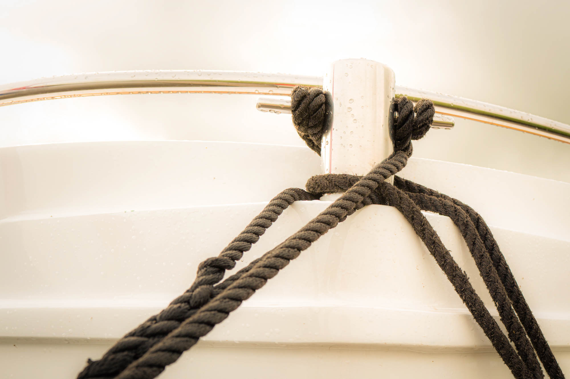 Close-up of braided rope tied to a shiny cleat on a boat, showing nautical details and marine hardware.