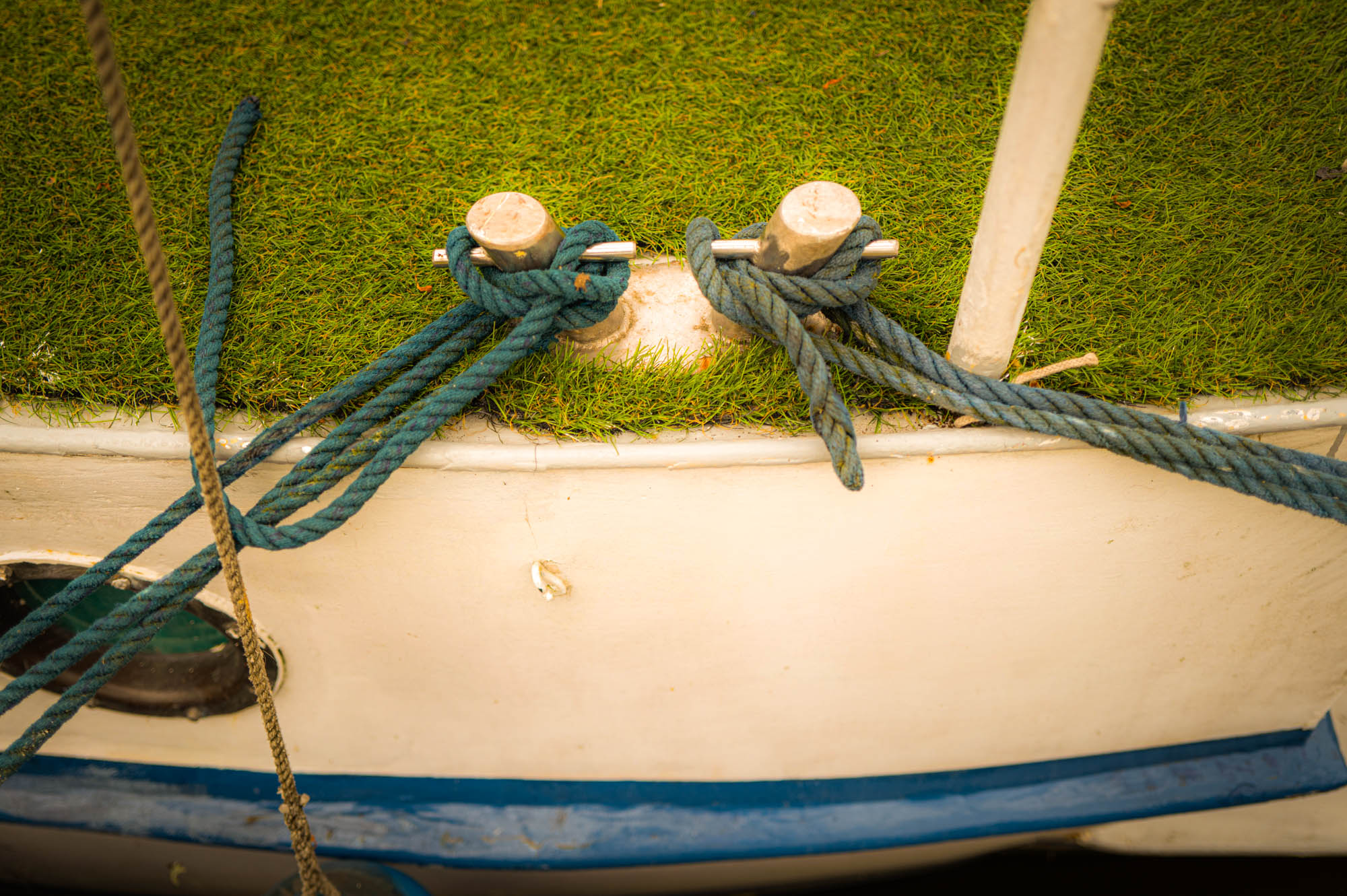 Boat deck with artificial grass and blue ropes tied to cleats.