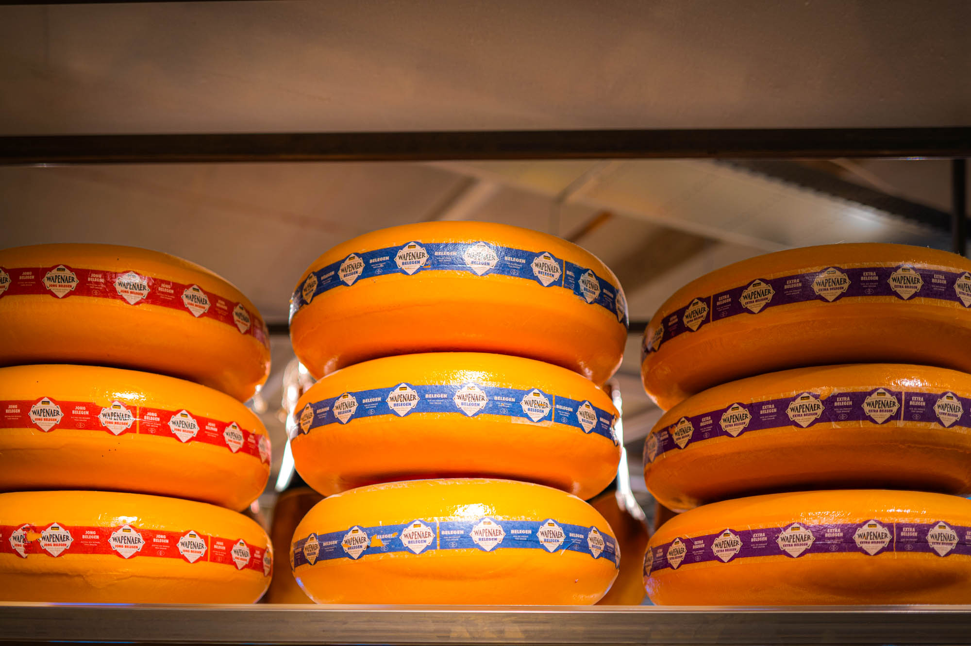 Stacks of Gouda cheese wheels with colorful labels in a cheese shop display.