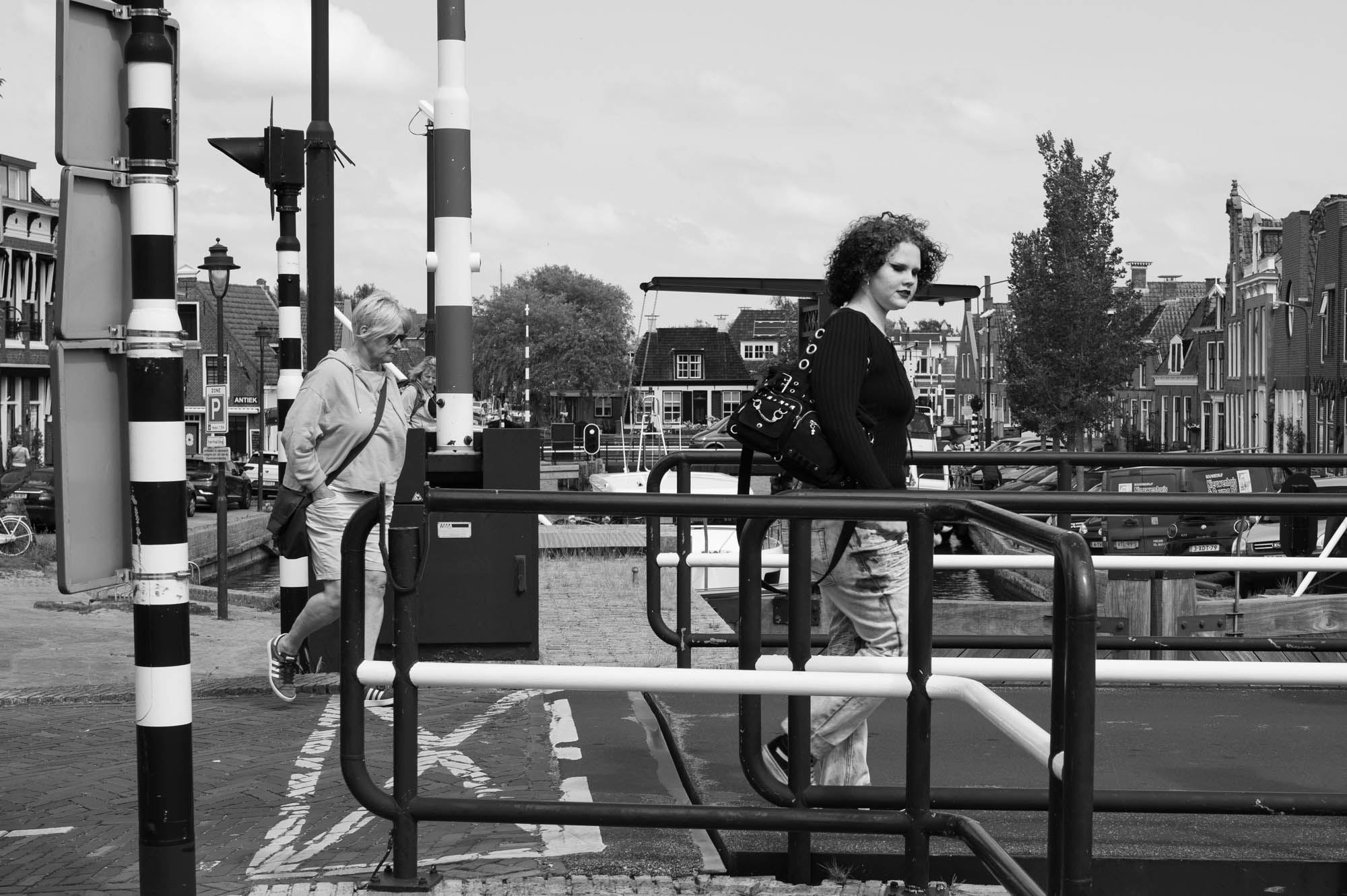 People walking on a bridge in a European city, with canal houses and street signs. Black and white photo.