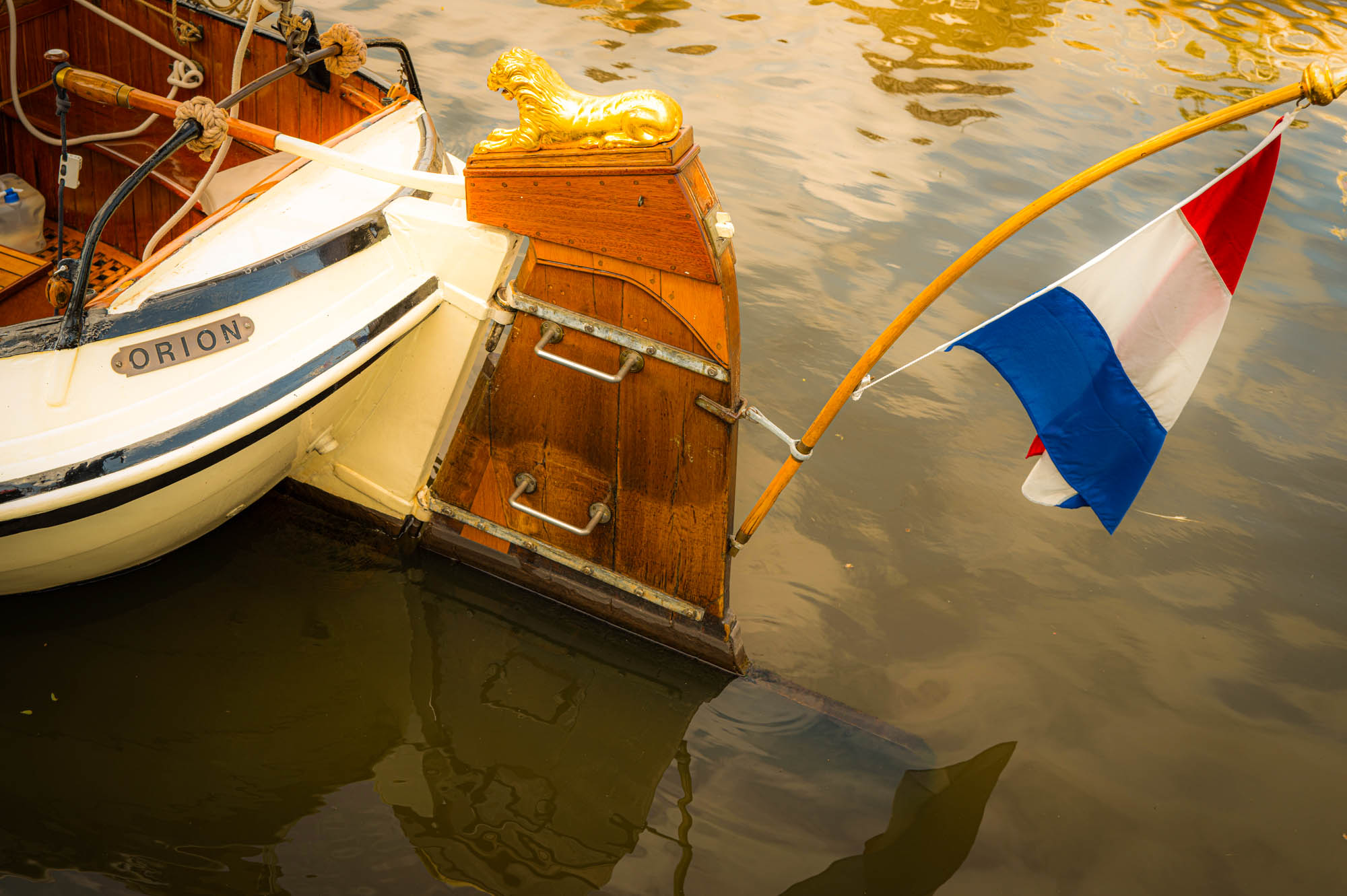 Close-up of boat stern with golden lion and Dutch flag in water reflection.