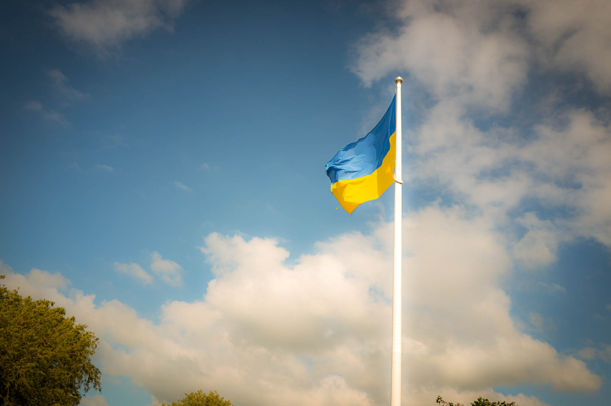 Ukrainian flag waving on a tall pole against a blue sky with clouds.
