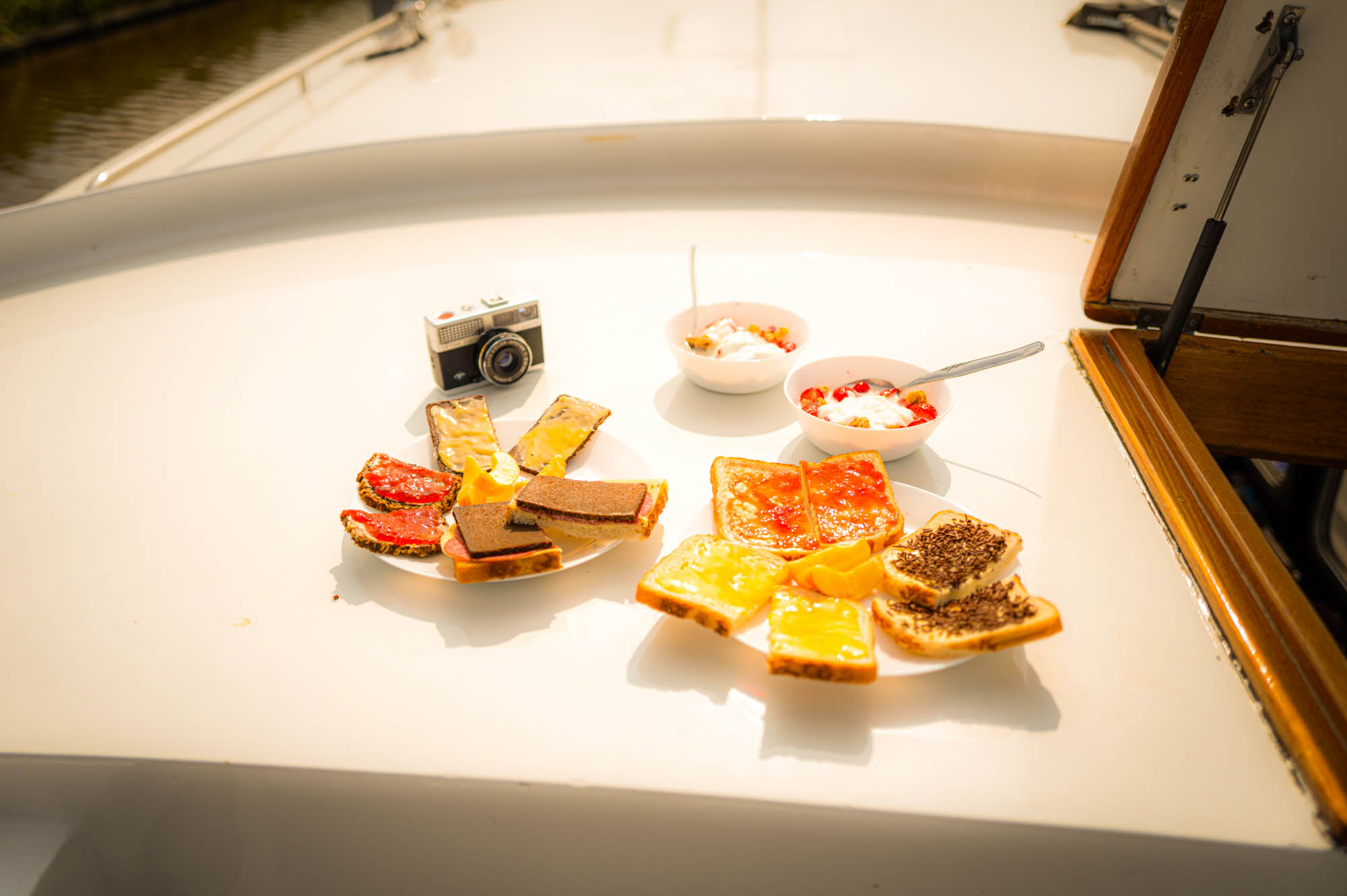 Breakfast on a boat with yogurt bowls, toast, and a vintage camera on a sunny day.