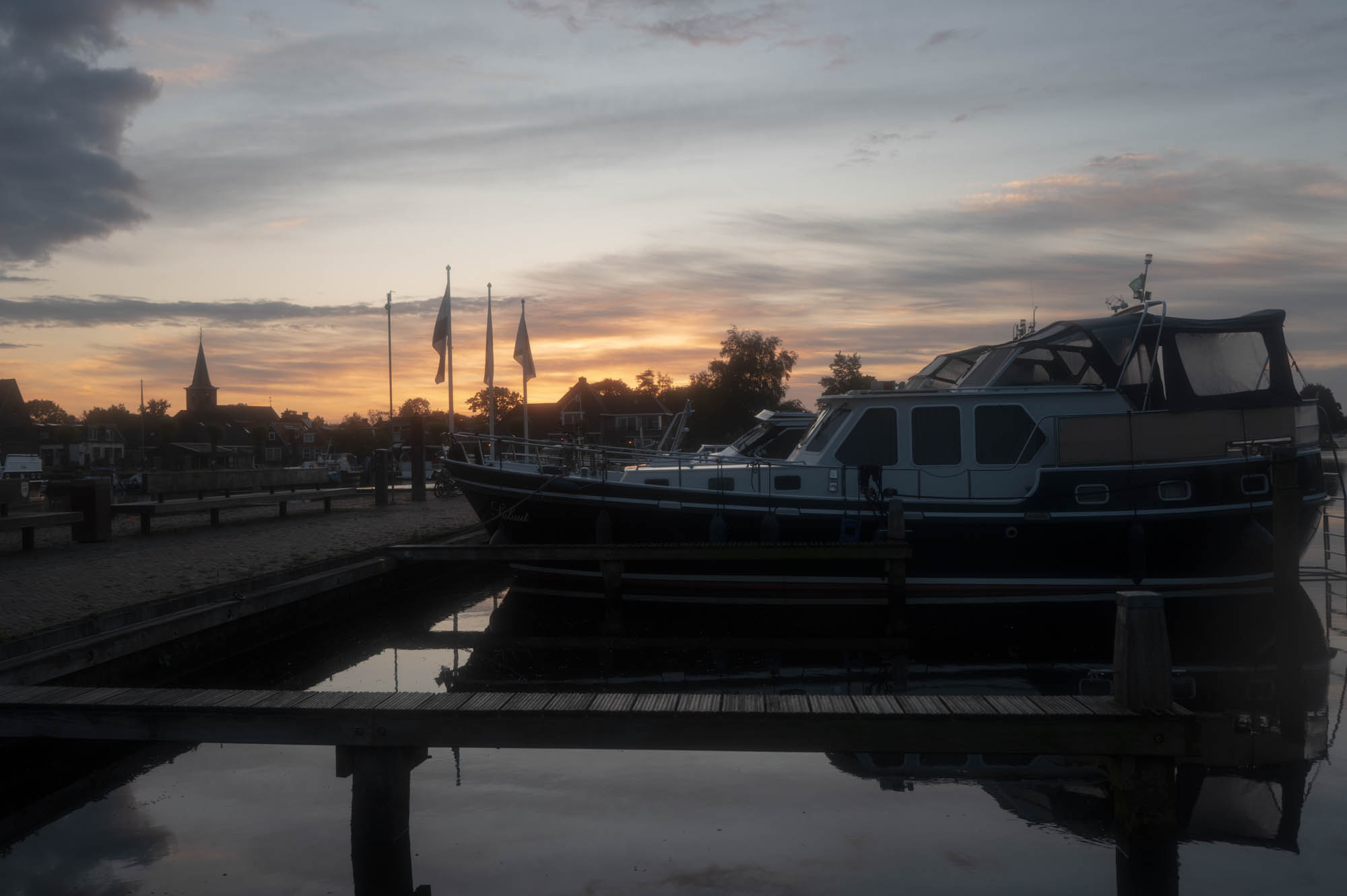 Sunset over a tranquil harbor with boats and a church spire silhouetted in the background.