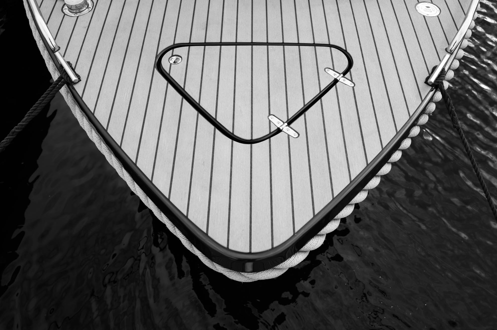 Close-up of a boat deck with wooden planks and a triangular hatch over dark water.