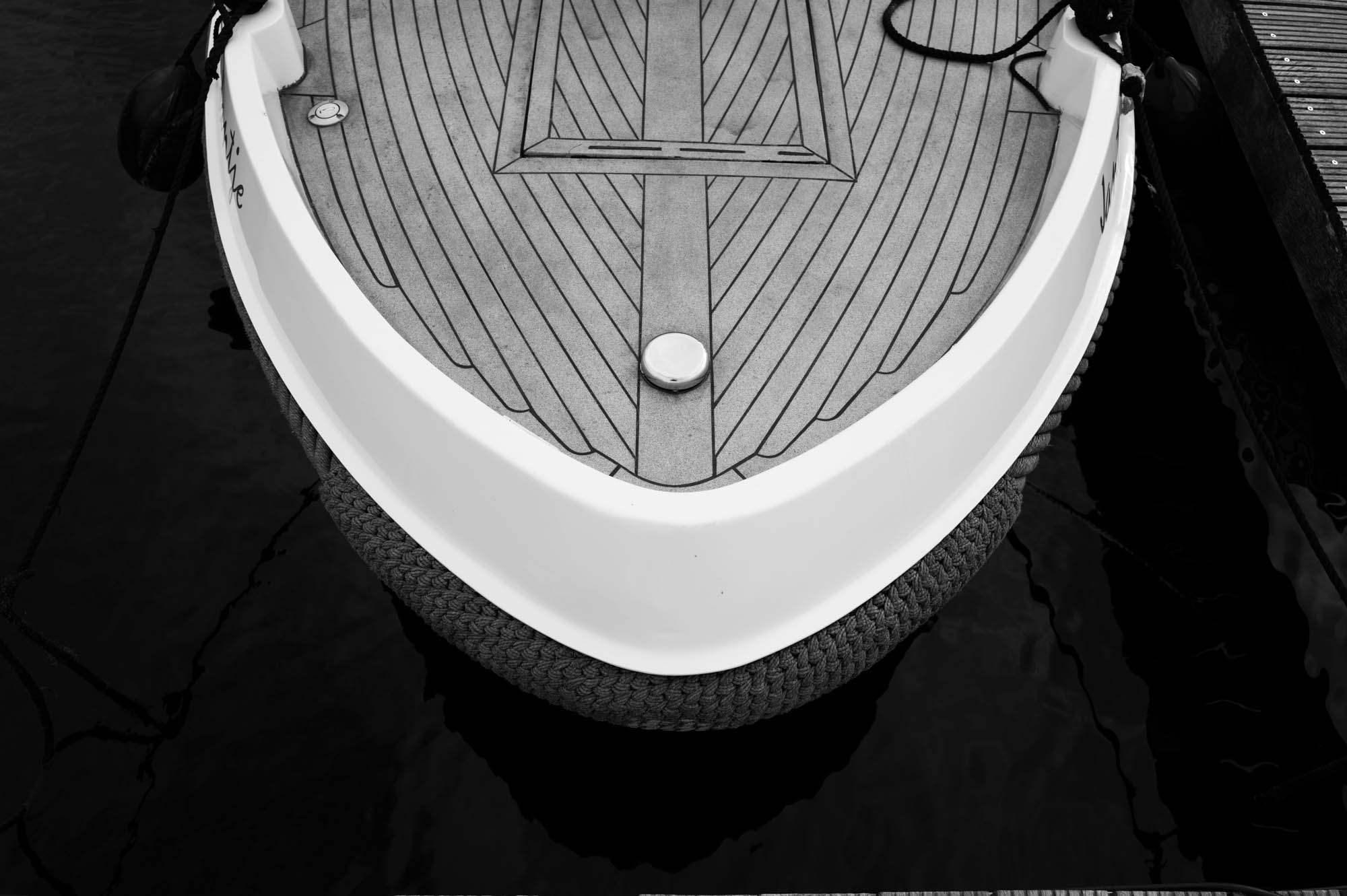 Black and white image of a boat's bow with a sleek design, docked in calm water.