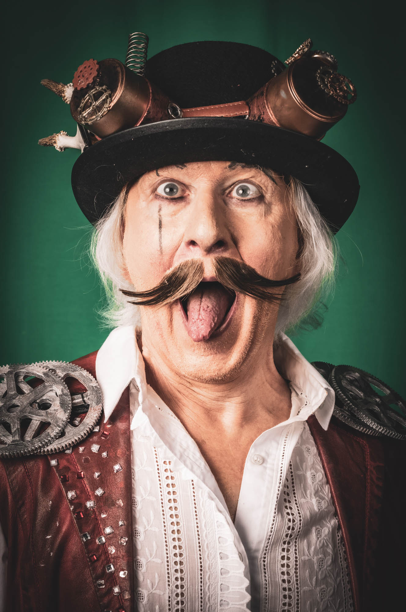 Steampunk man with a top hat, gears, and mustache making a funny expression against a green background.