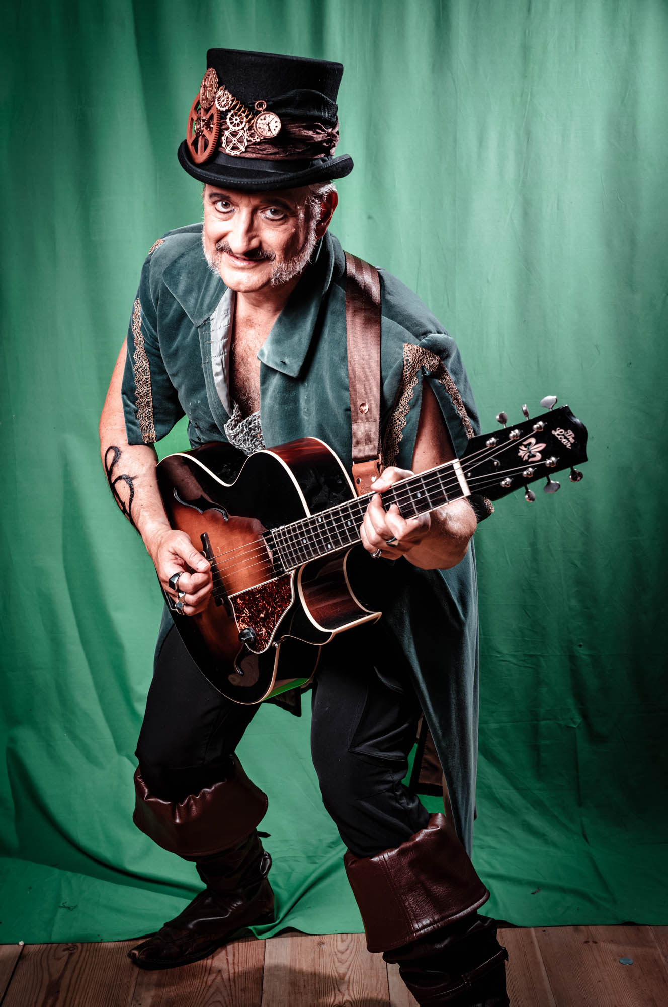 Steampunk musician with guitar, wearing a top hat with gears, stands against a green background.