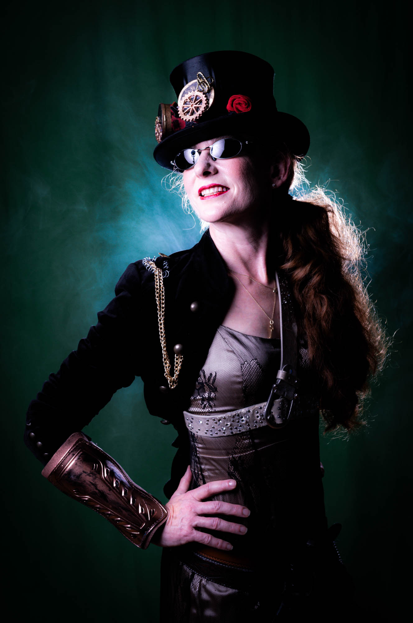 Steampunk fashion: woman in top hat and goggles, brass accessories, green background.