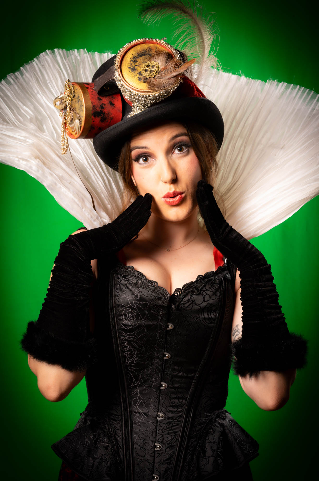 Steampunk woman in vintage black corset, feathered hat, and gloves against a green background, posing with a surprised expression.