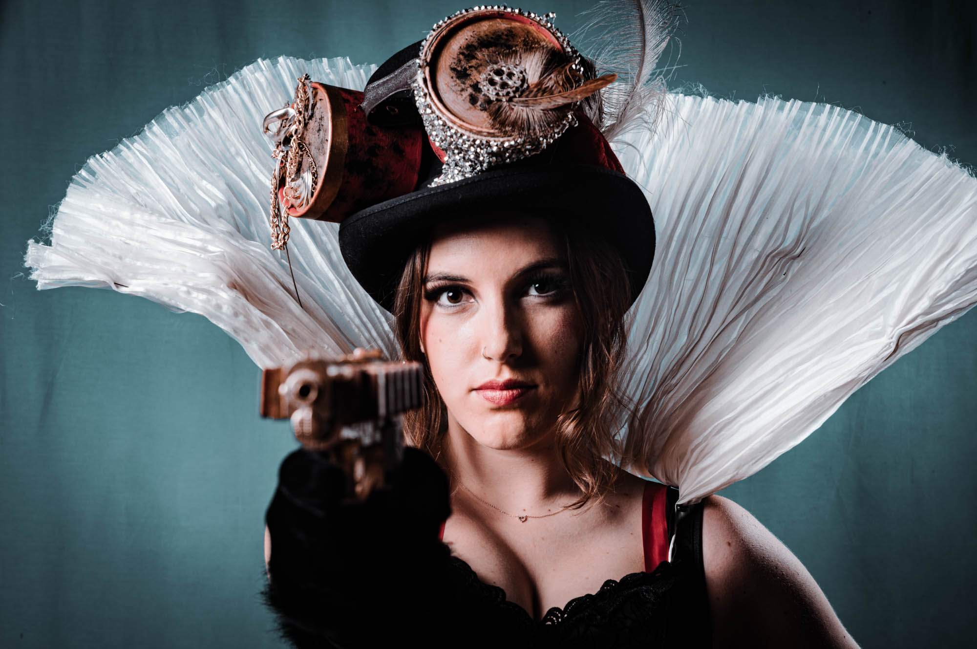 Steampunk-inspired woman with a decorative top hat and ruffled collar points a vintage-style gun at the camera.