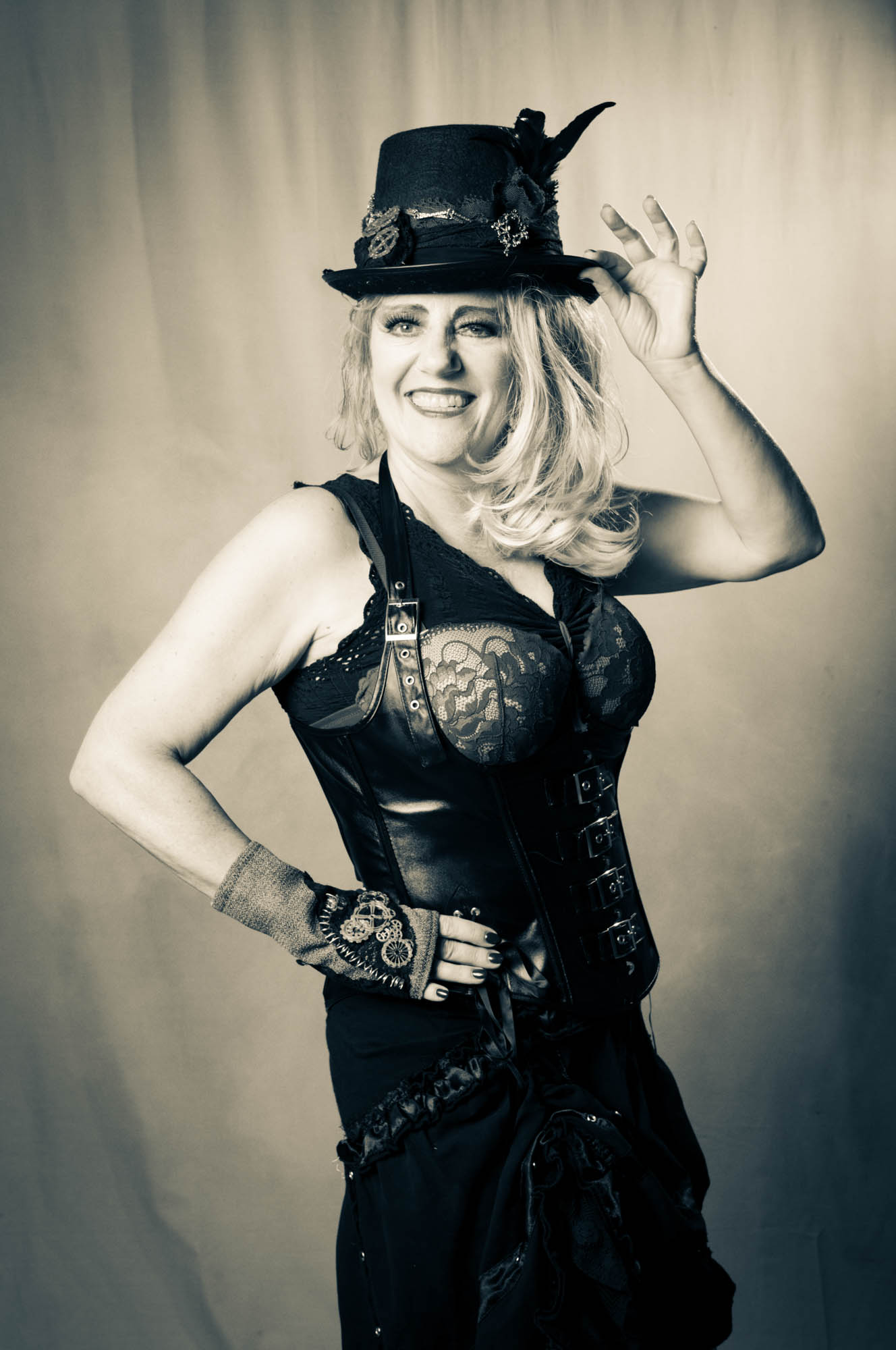 Smiling woman in steampunk attire with lace corset and decorated top hat, set against a soft blurred background.