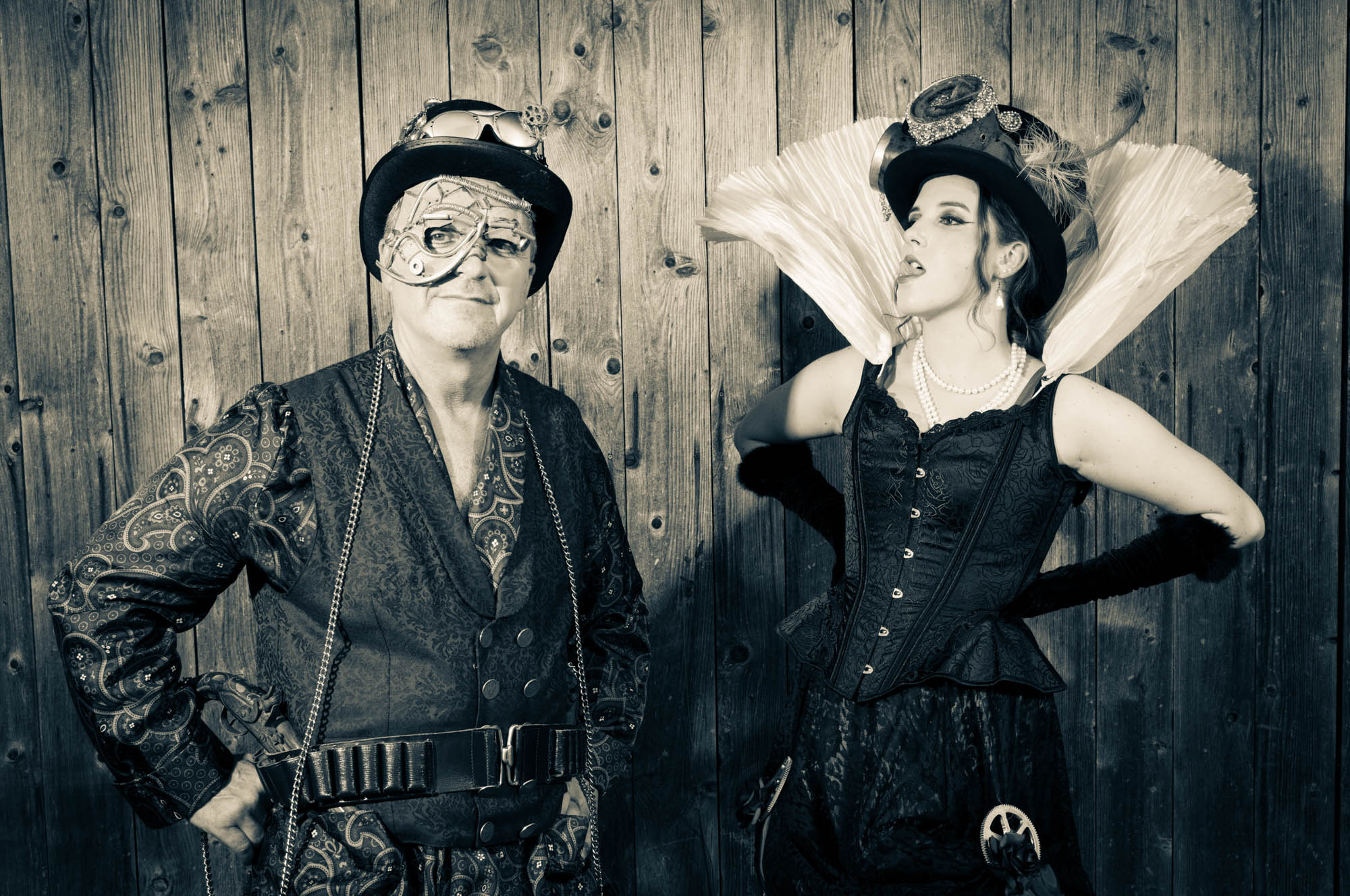 Steampunk enthusiasts in vintage attire against wooden backdrop, showcasing unique hats and intricate masks.