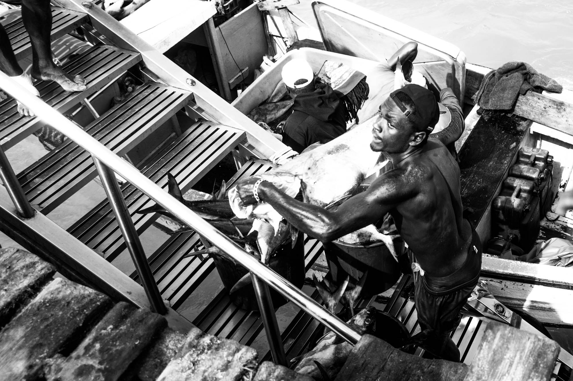 Fisherman carrying large fish on a fishing boat, captured in black and white, showcasing the hard work of fishing.
