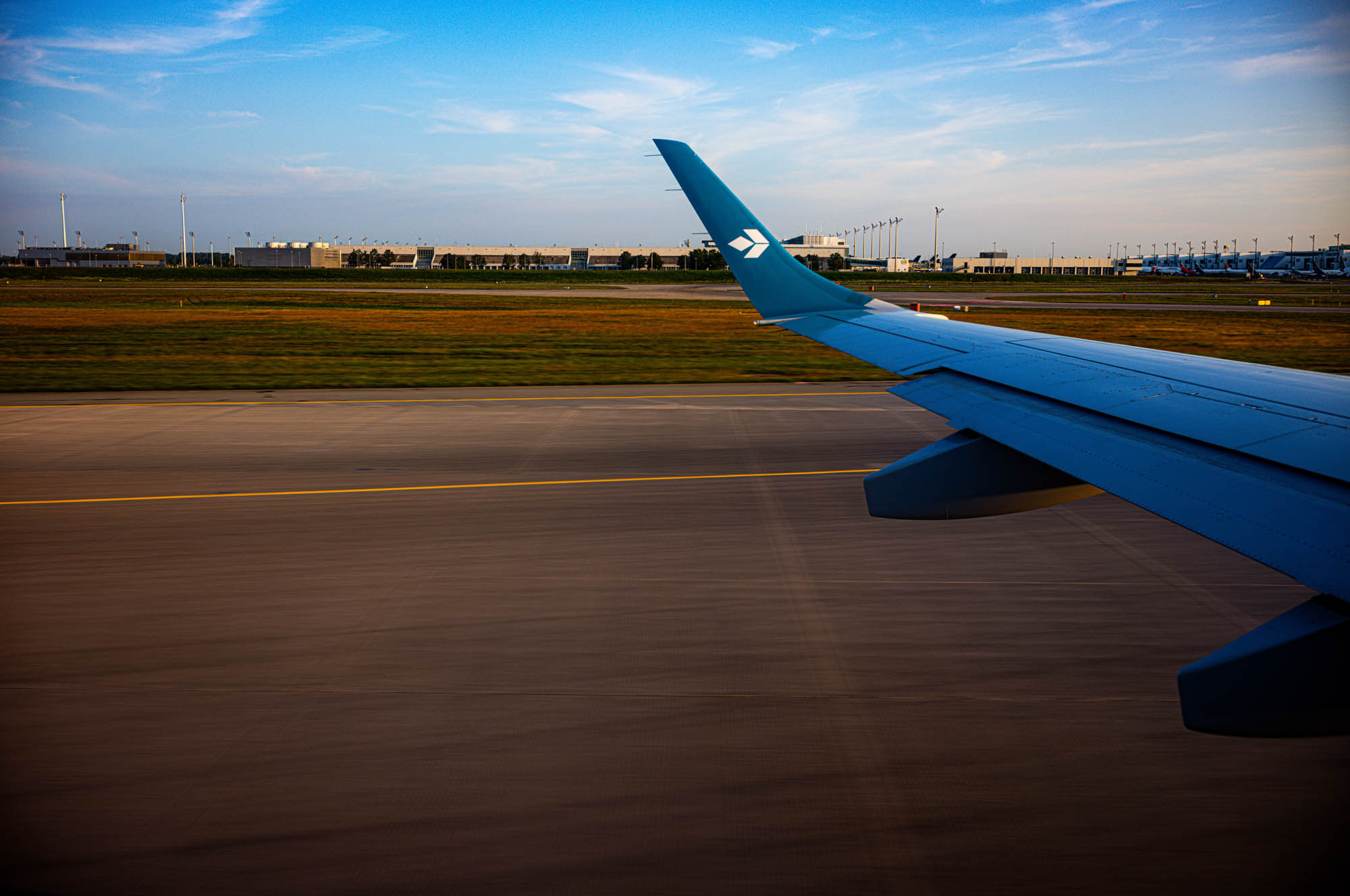 Airplane wing view from window during taxiing at the airport runway, clear sky and tarmac visible.