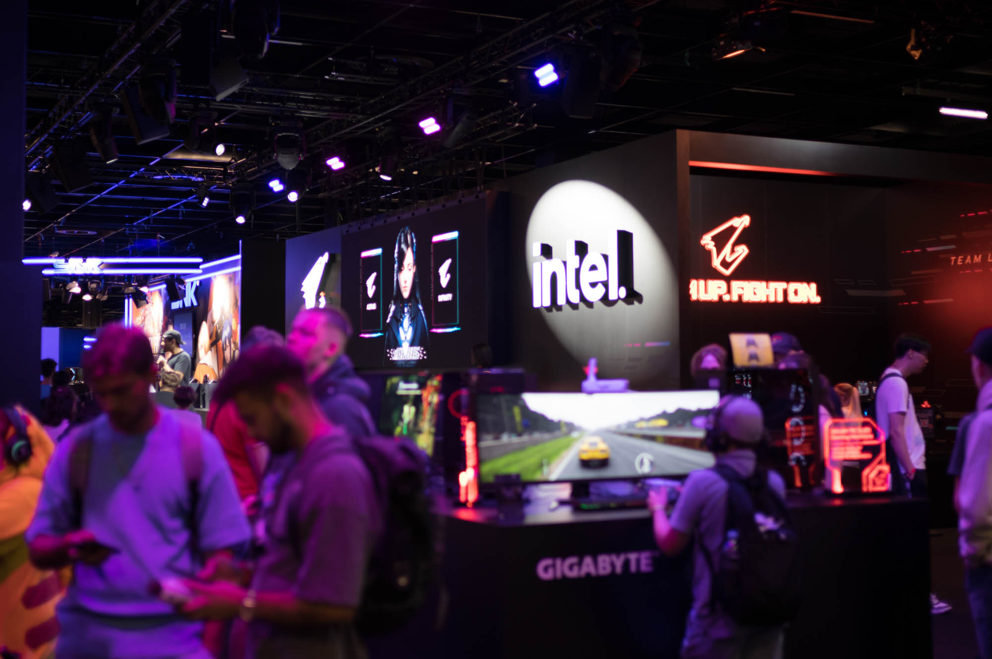 People attending a tech event with Intel and Gigabyte displays in a vibrant, neon-lit atmosphere.