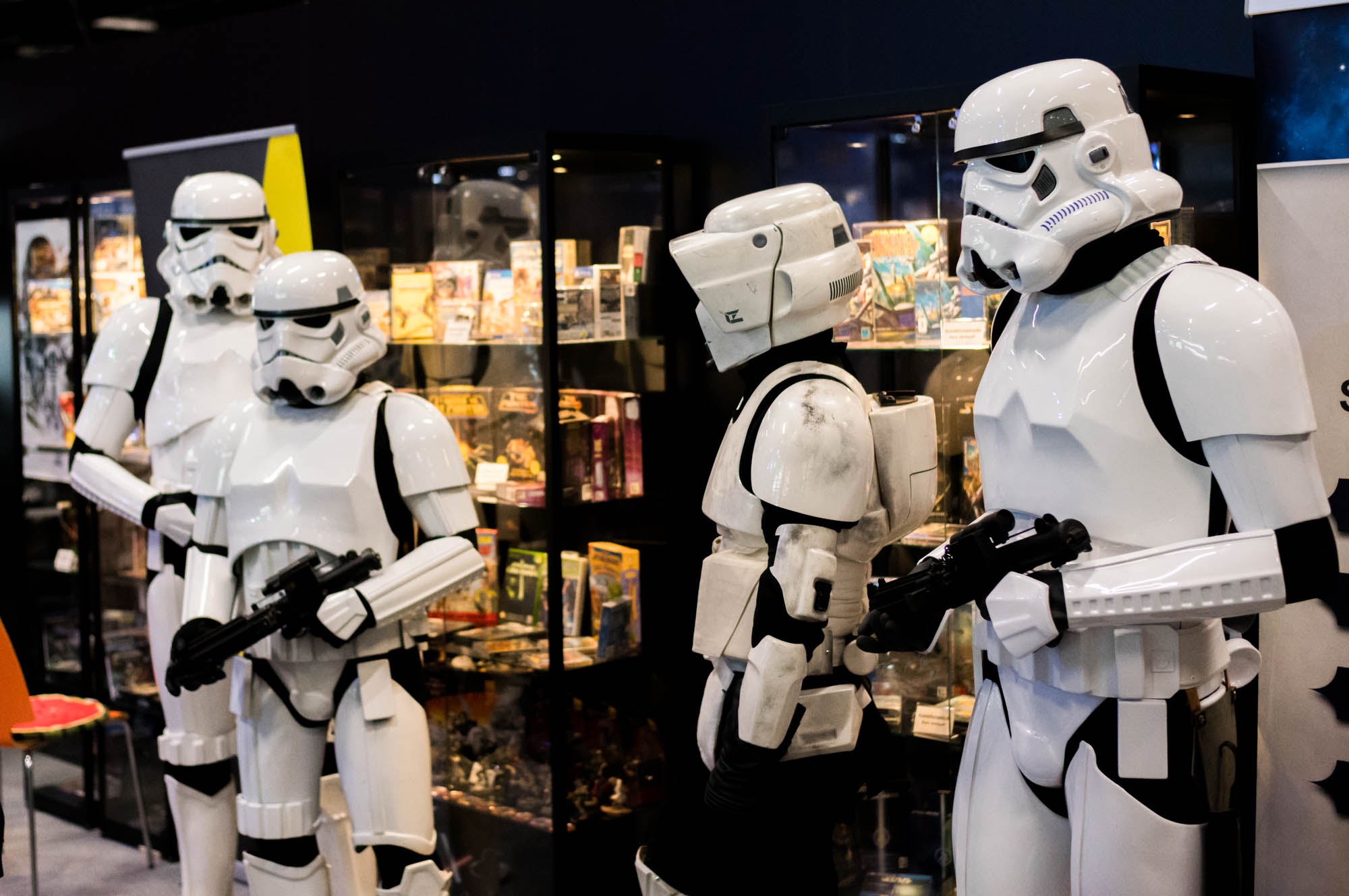 Four people in Stormtrooper costumes stand in front of display cases at a sci-fi convention.
