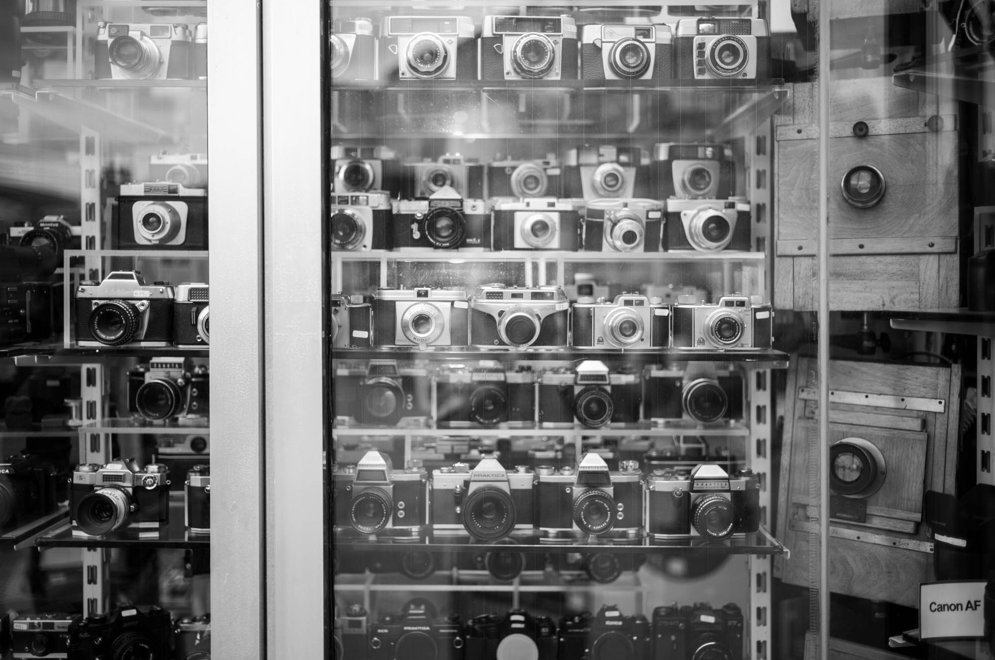 Black and white photo of a vintage camera collection in a display cabinet.